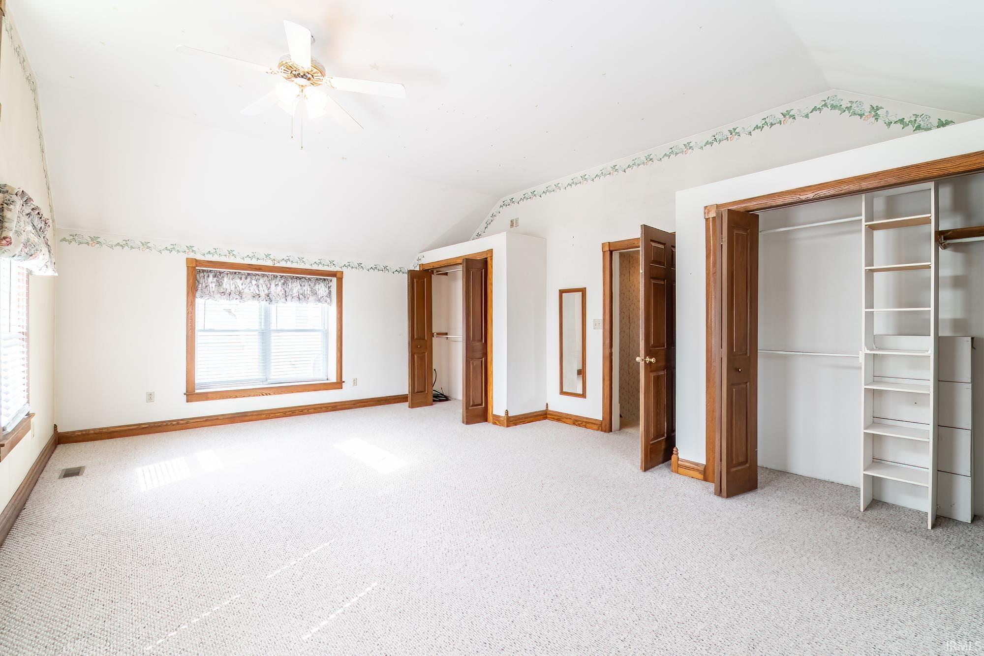 Primary bedroom featuring vaulted ceiling, light colored carpet, ceiling fan, and multiple closets
