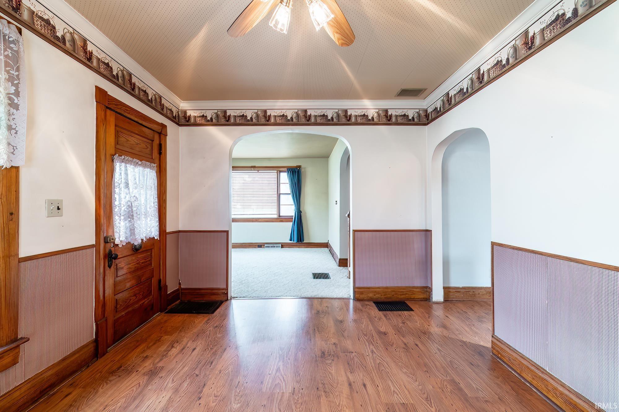 Entrance foyer featuring a wainscoted wall, a ceiling fan, wood finished floors, wooden walls, and crown molding