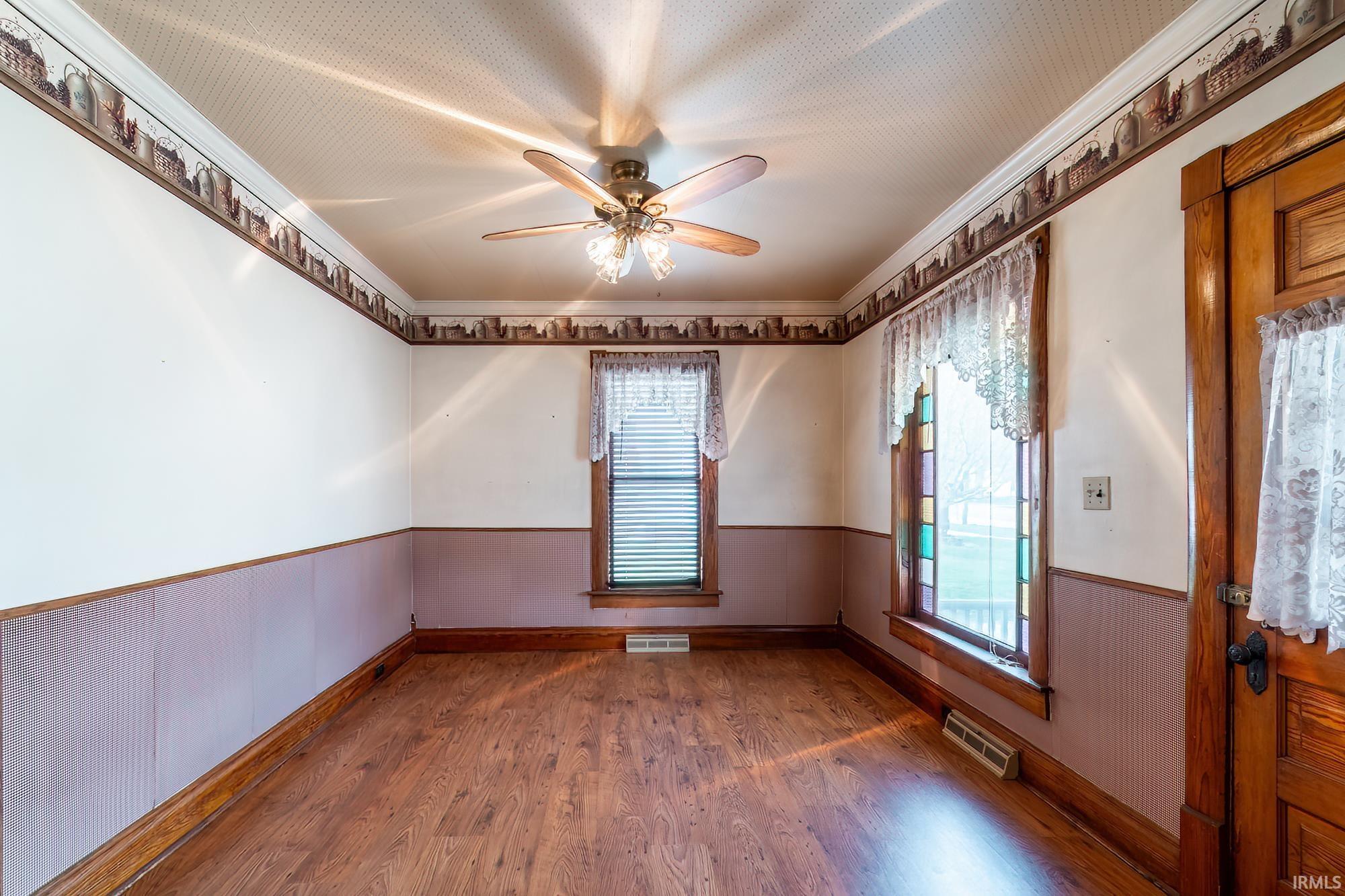 Dining Room featuring a wainscoted wall, dark wood-style floors, a ceiling fan, ornamental molding, and wooden walls