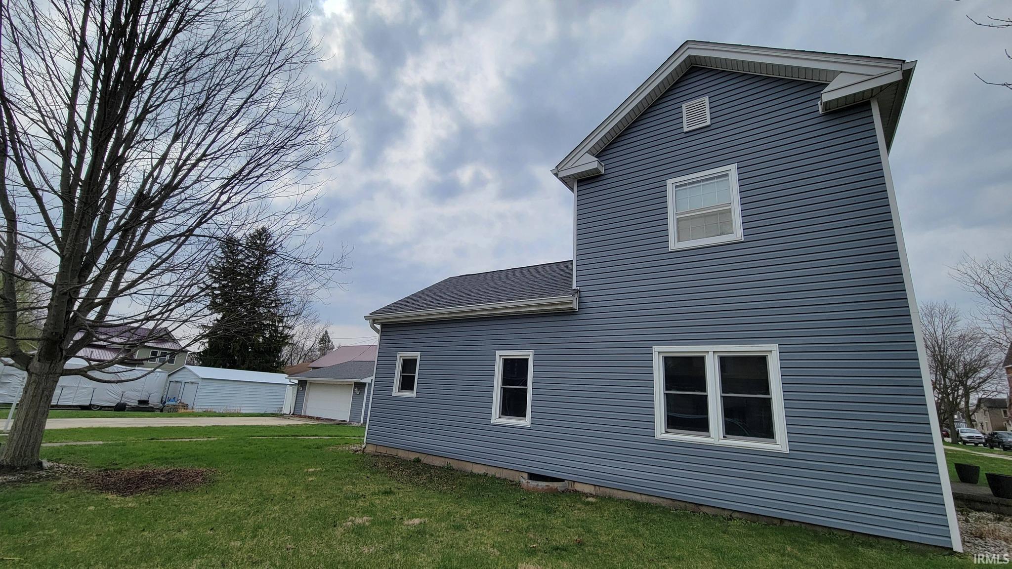 Back of property featuring a lawn, roof with shingles, and an outdoor structure