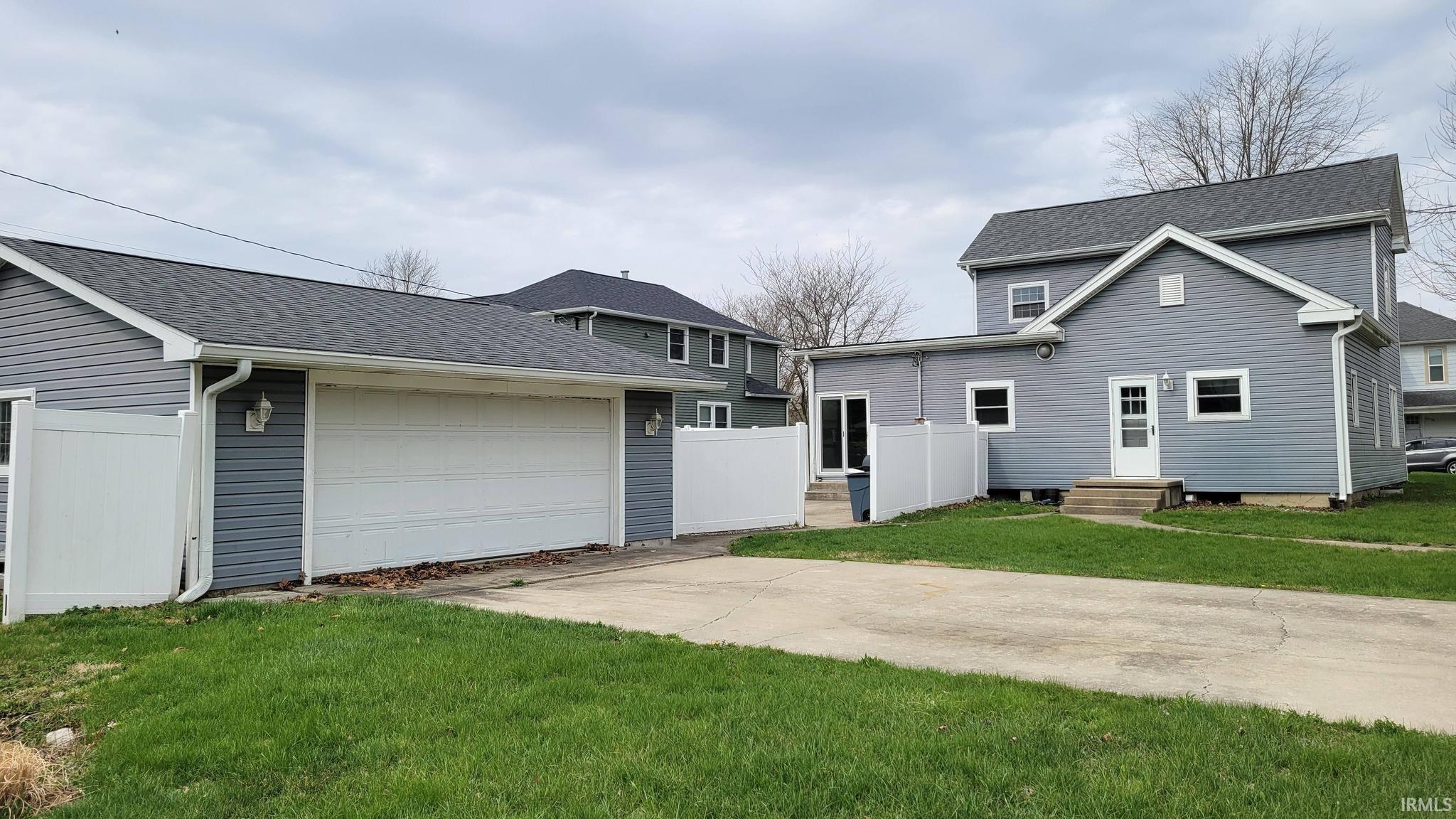 Rear view of house featuring a shingled roof, an outbuilding, concrete driveway, an attached garage, and entry steps
