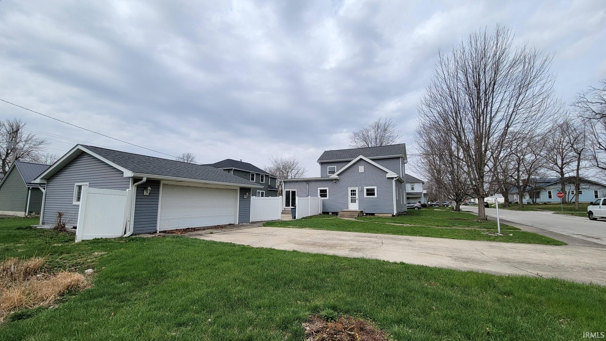 View of front of home with a front yard, an outbuilding, concrete driveway, an attached garage, and a shingled roof