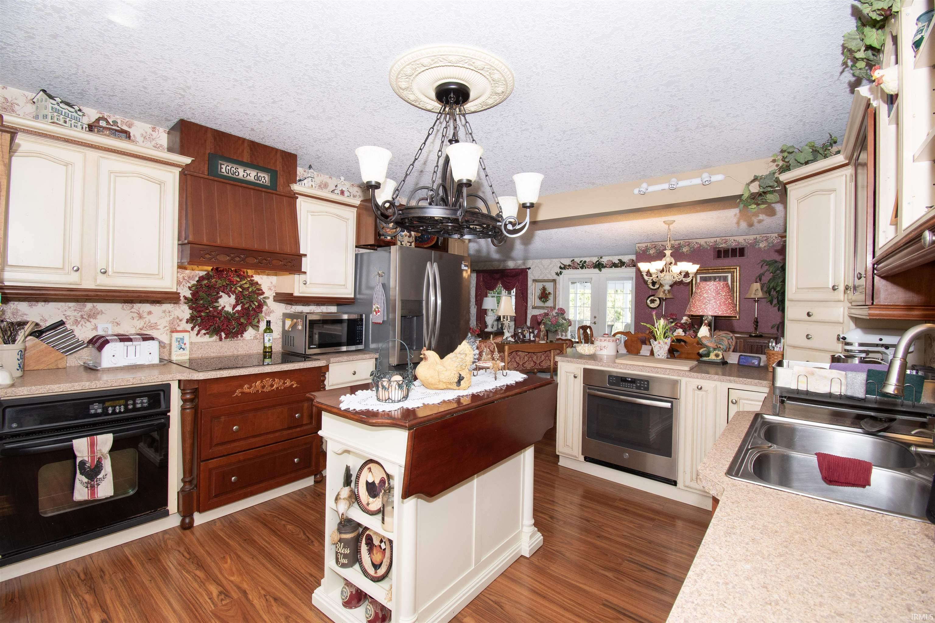 Kitchen with black appliances, a textured ceiling, hanging lights, wallpapered walls, and dark wood finished floors