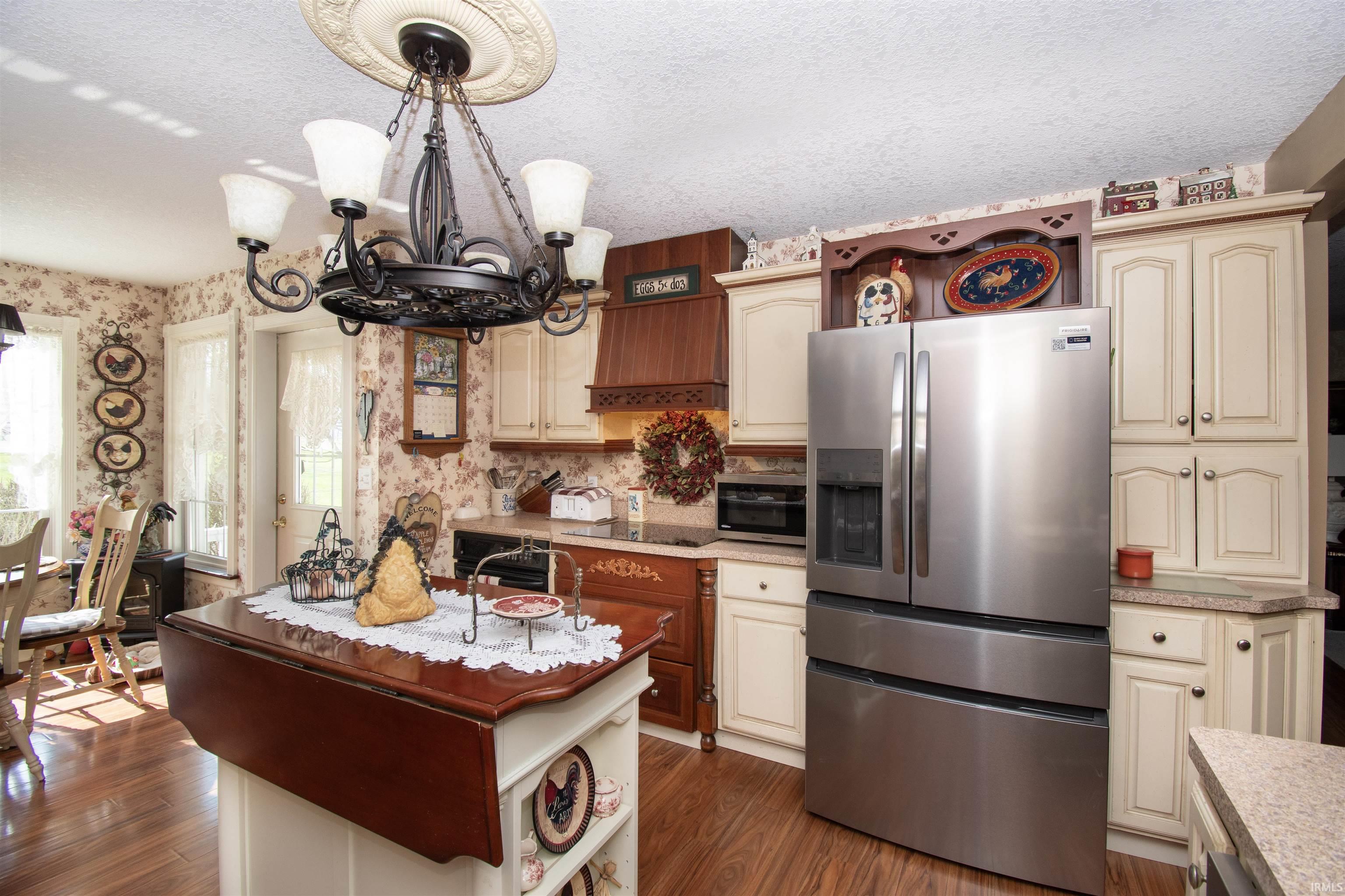 Kitchen with stainless steel appliances, light countertops, dark wood-style floors, cream cabinetry, and wallpapered walls