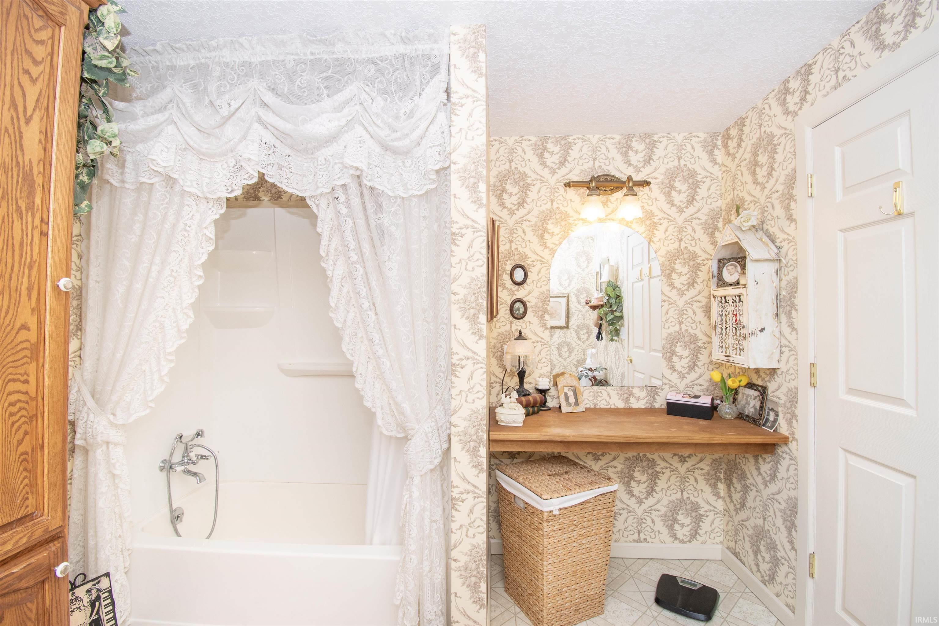 Bathroom featuring wallpapered walls, shower / tub combo with curtain, vanity, a textured ceiling, and tile patterned flooring