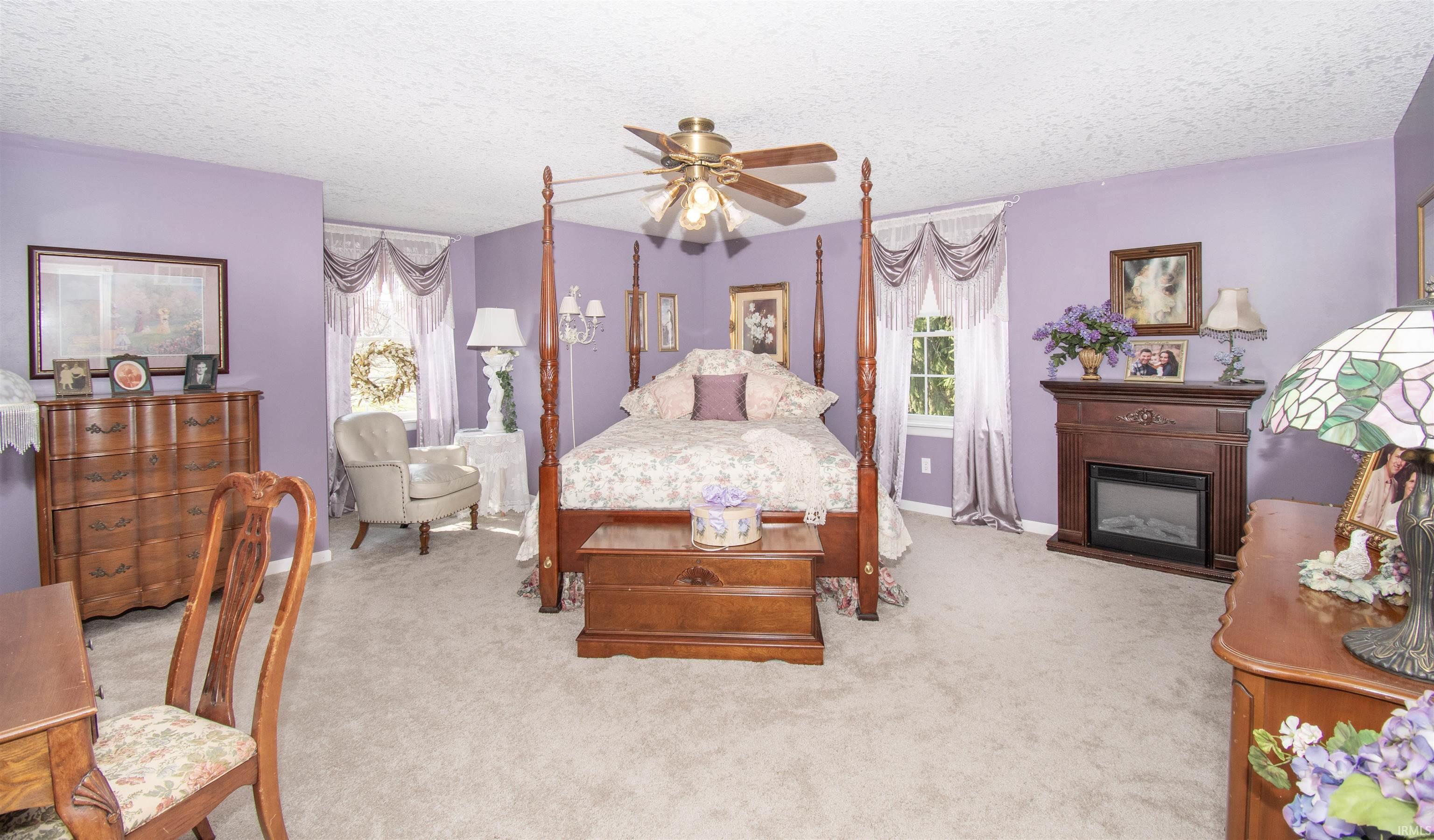 Bedroom featuring light carpet, a glass covered fireplace, a textured ceiling, ceiling fan, and multiple windows