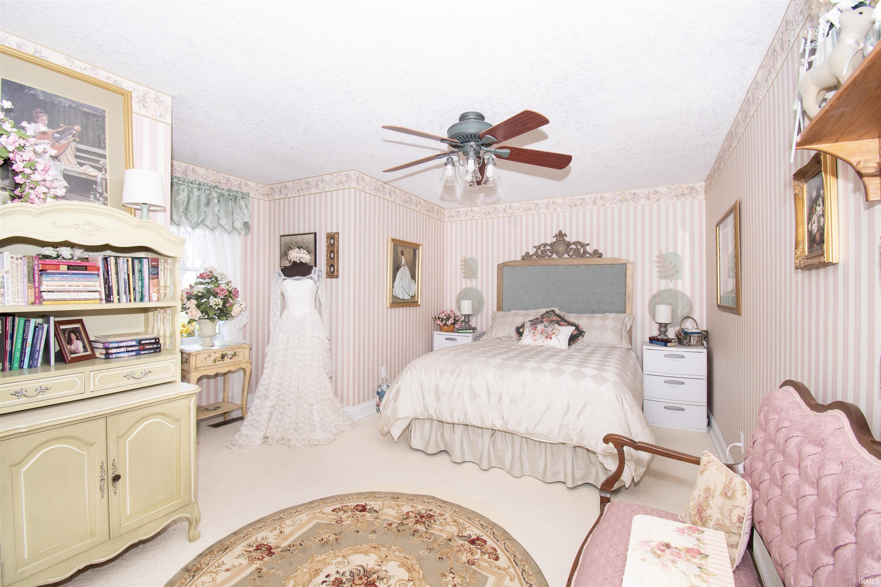 Bedroom featuring a textured ceiling, wallpapered walls, light colored carpet, and a ceiling fan