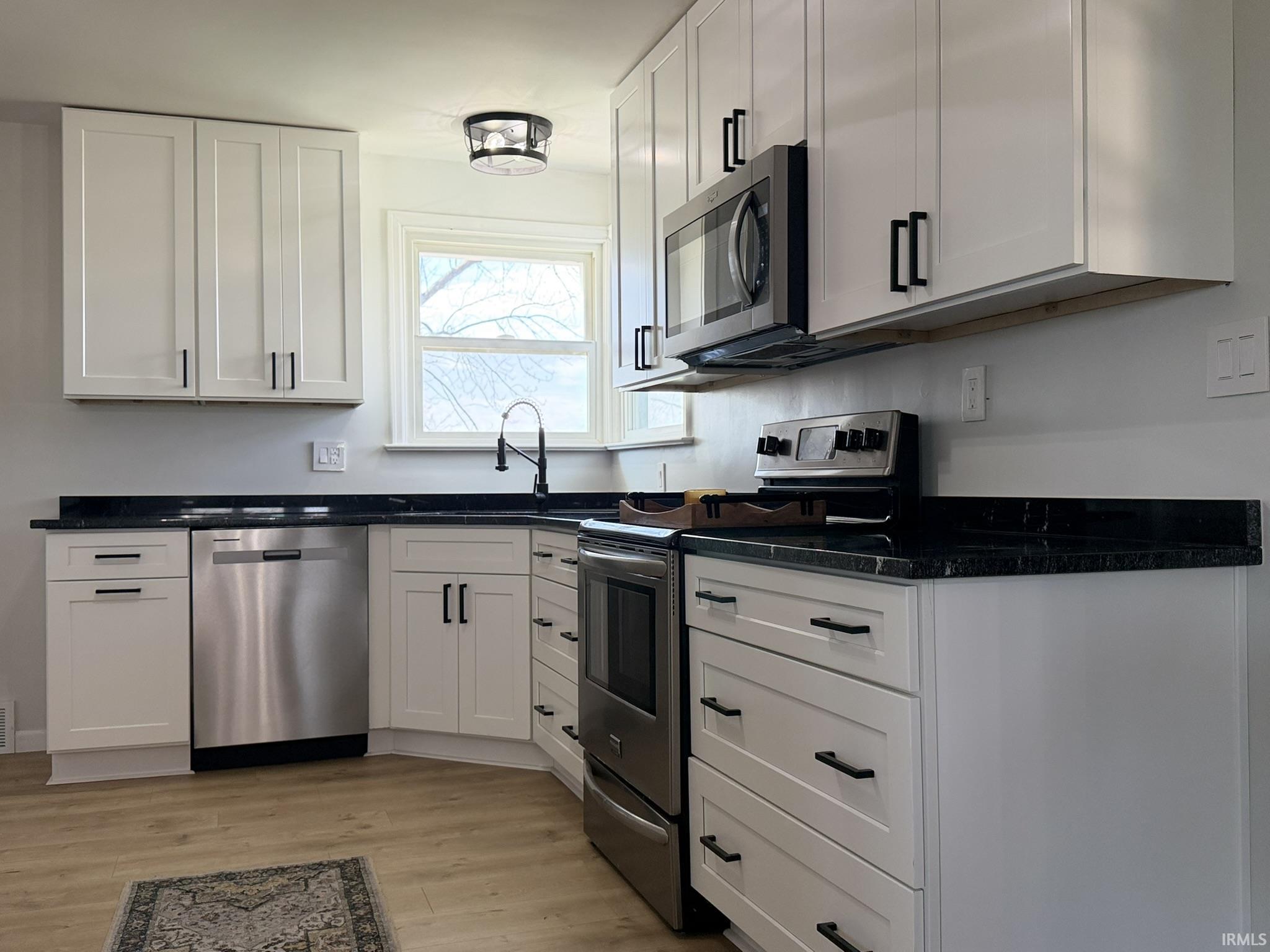Kitchen featuring stainless steel appliances, white cabinets, light wood-type flooring, and dark stone counters
