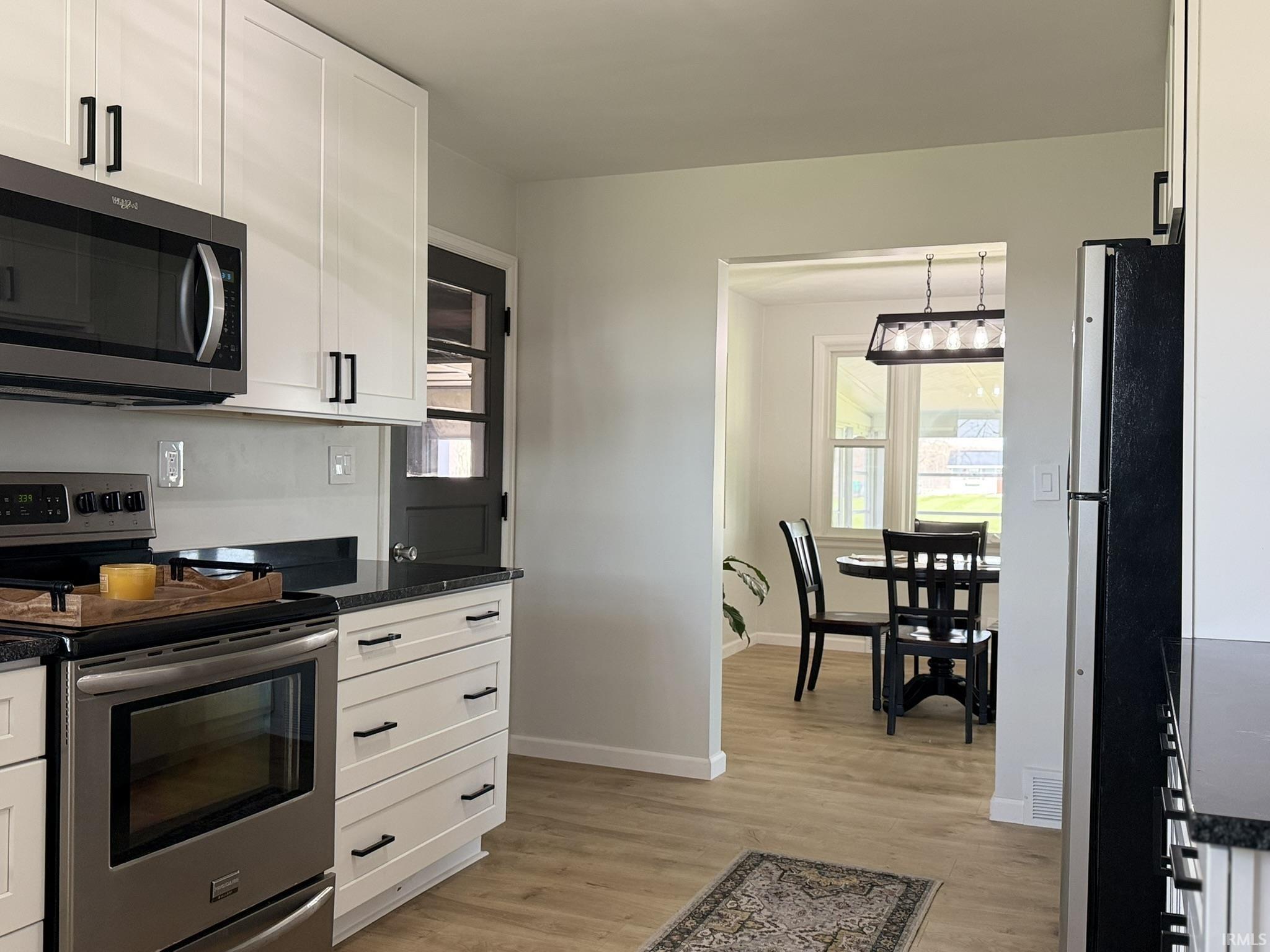 Kitchen with stainless steel appliances, white cabinets, light wood finished floors, and healthy amount of natural light