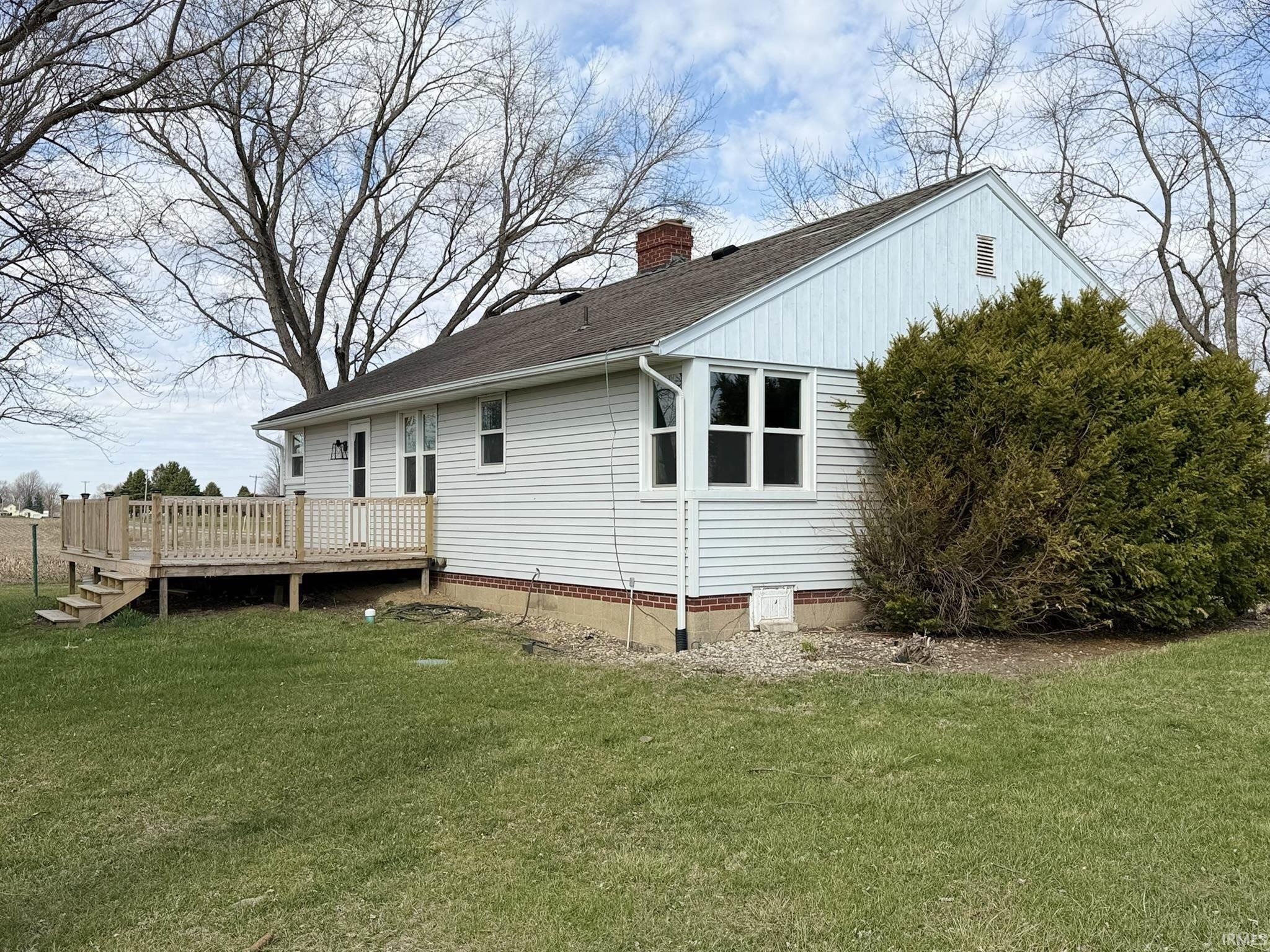 Rear view of property featuring a wooden deck, a lawn, a chimney, and a shingled roof