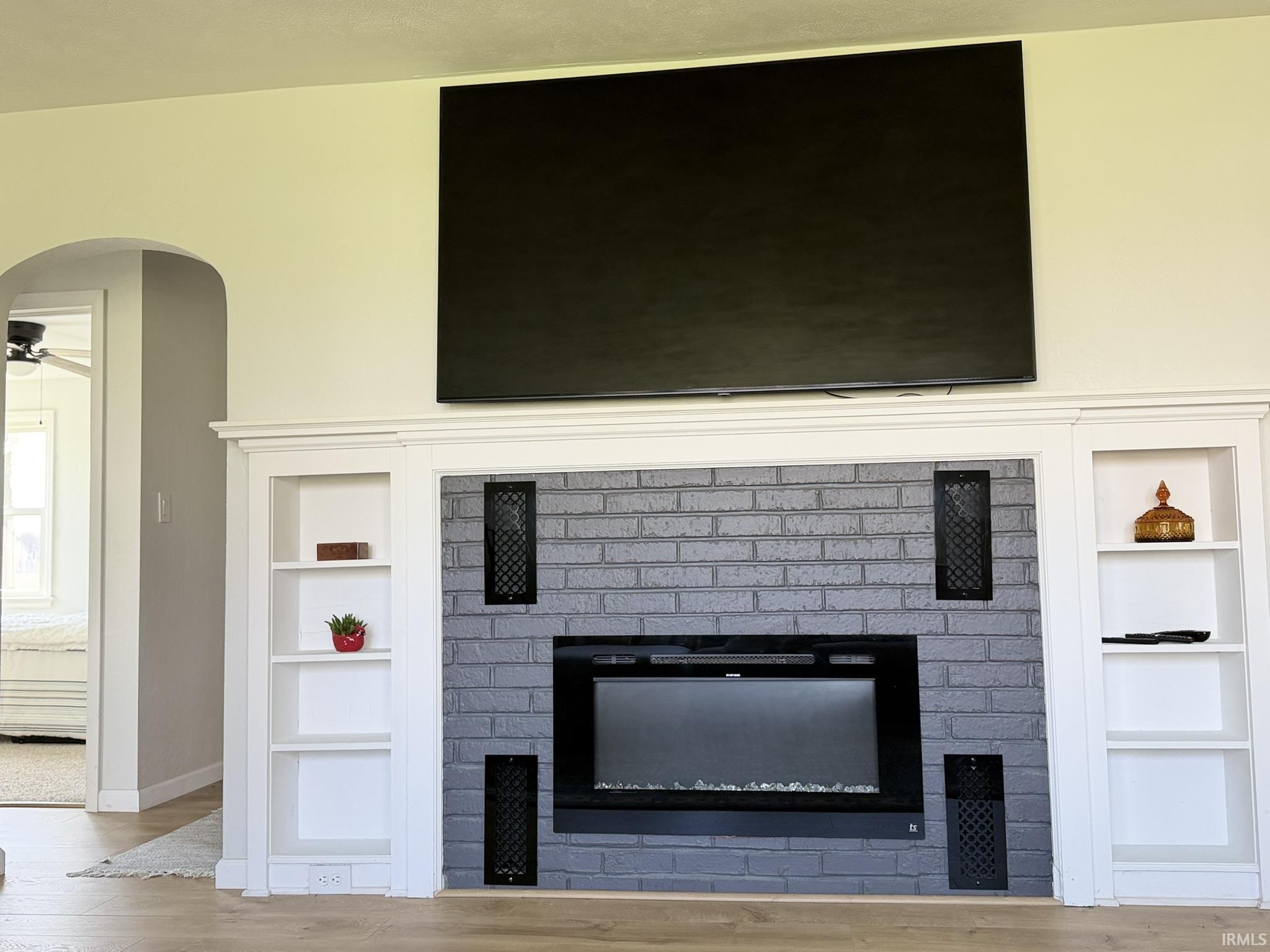 Detailed view of arched walkways, a brick fireplace, built in features, wood finished floors, and a ceiling fan