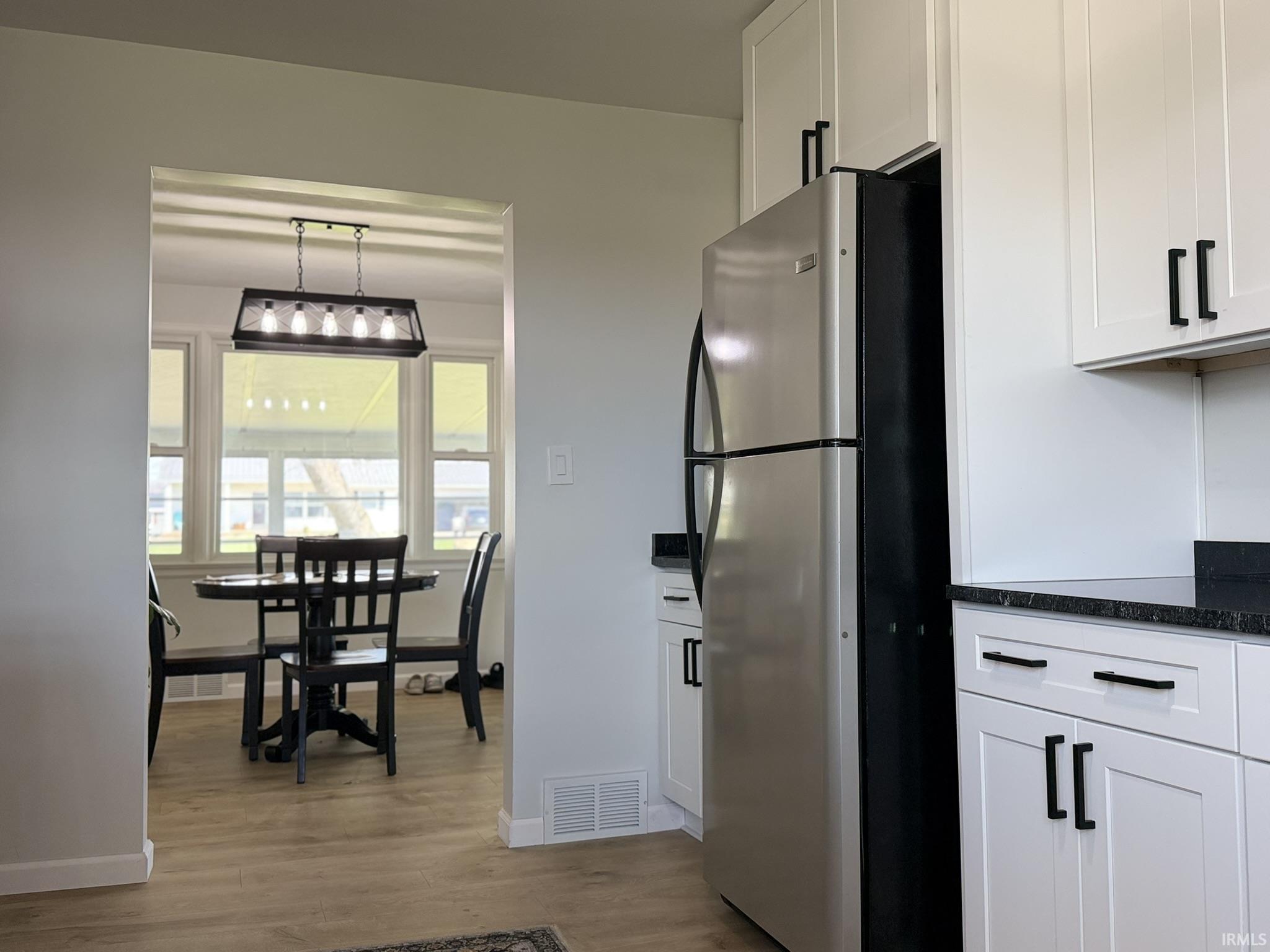 Kitchen featuring freestanding refrigerator, white cabinets, light wood finished floors, dark stone countertops, and decorative light fixtures