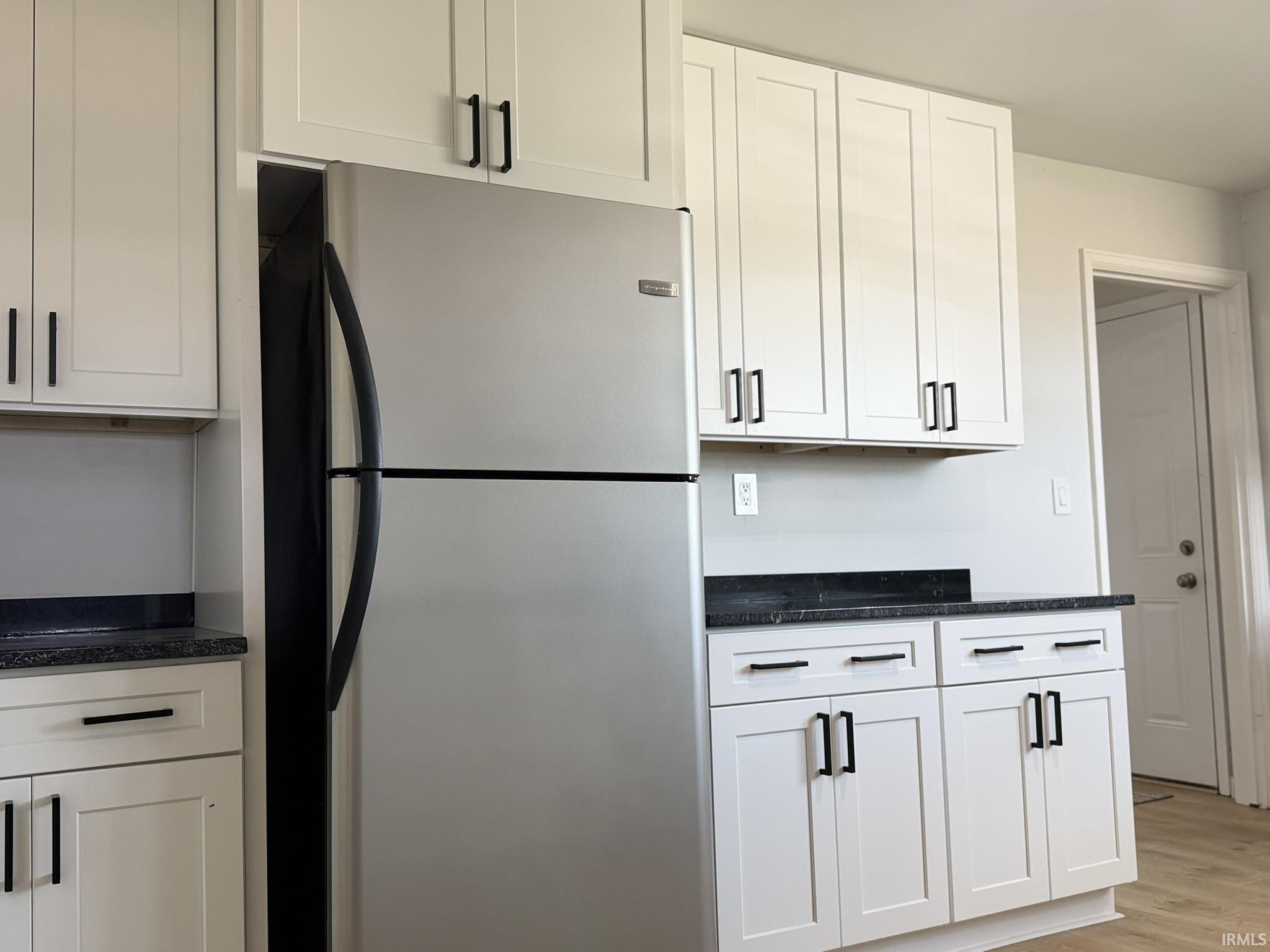 Kitchen with freestanding refrigerator, dark stone counters, white cabinetry, and light wood-style floors