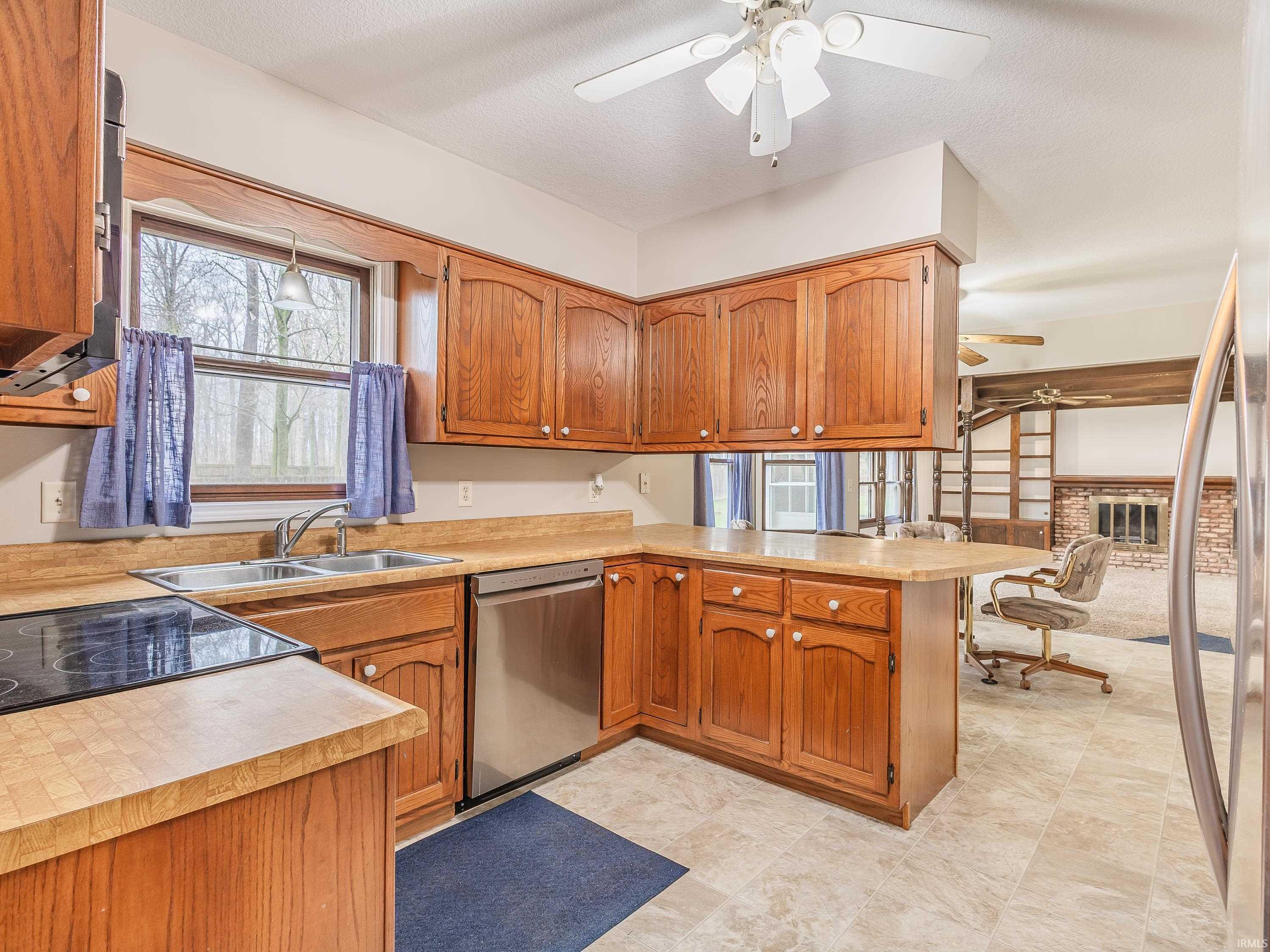 Kitchen with light countertops, a peninsula, ceiling fan, stainless steel appliances, and wood finish cabinetry