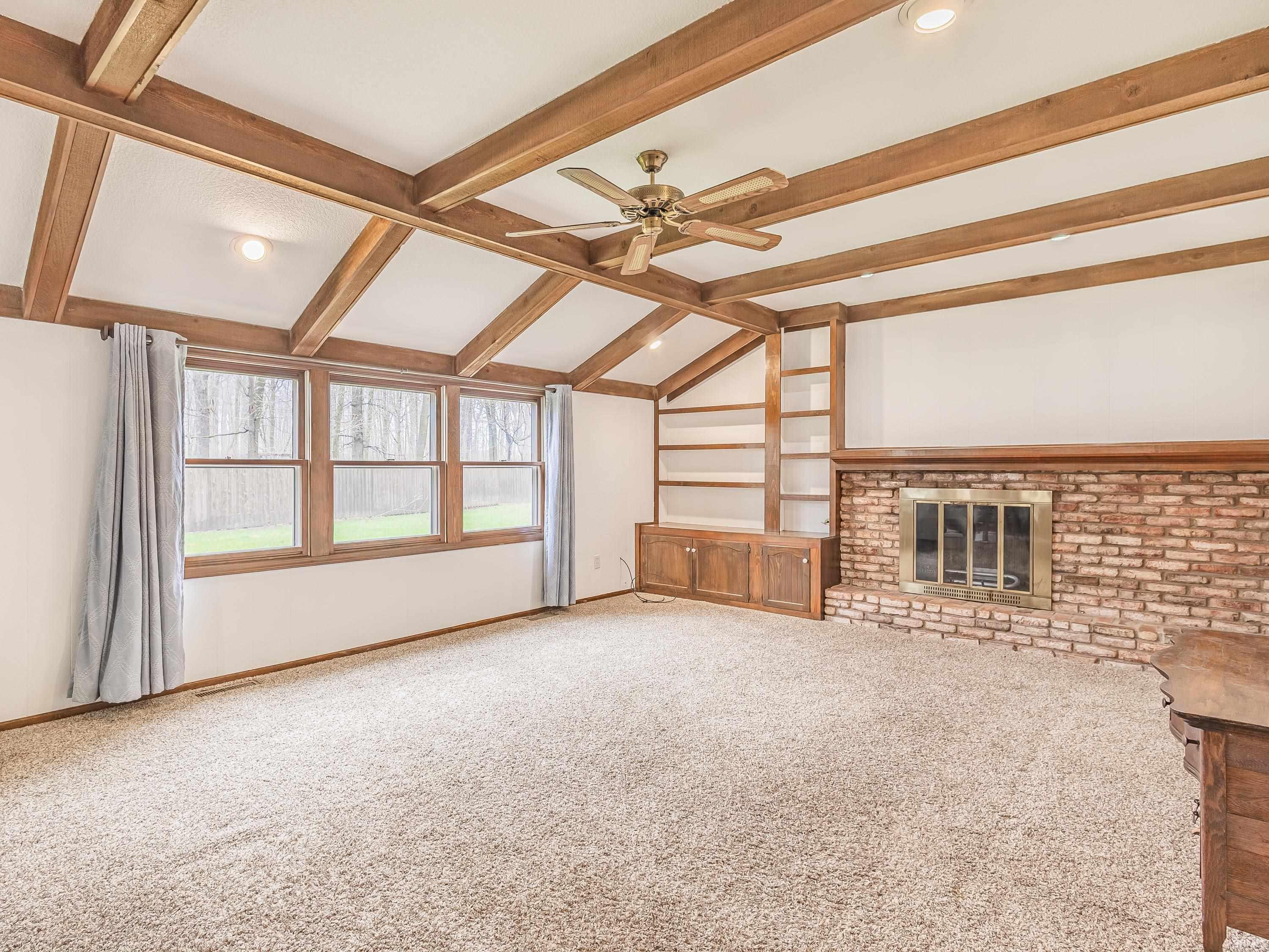 Family room featuring a ceiling fan, carpet, a brick gas fireplace, beamed ceiling, and built in shelves