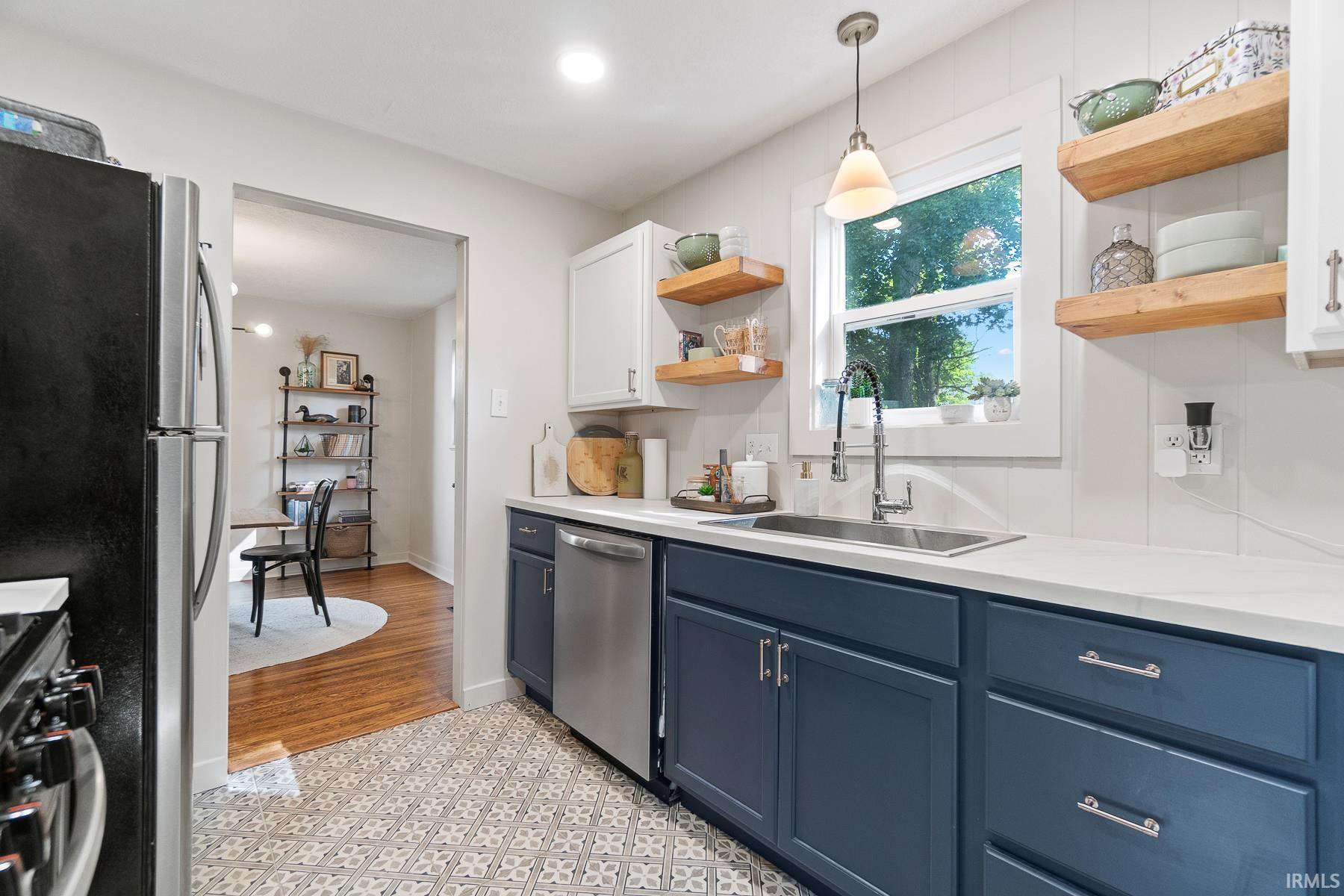 Two tone kitchen featuring stainless steel appliances, hanging light fixtures, open shelves, dual tone cabinetry, and light stone counters