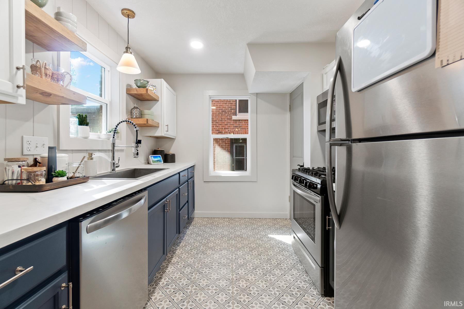 Two tone kitchen featuring stainless steel appliances, dual tone cabinets, open shelves, pendant lighting, and light floors