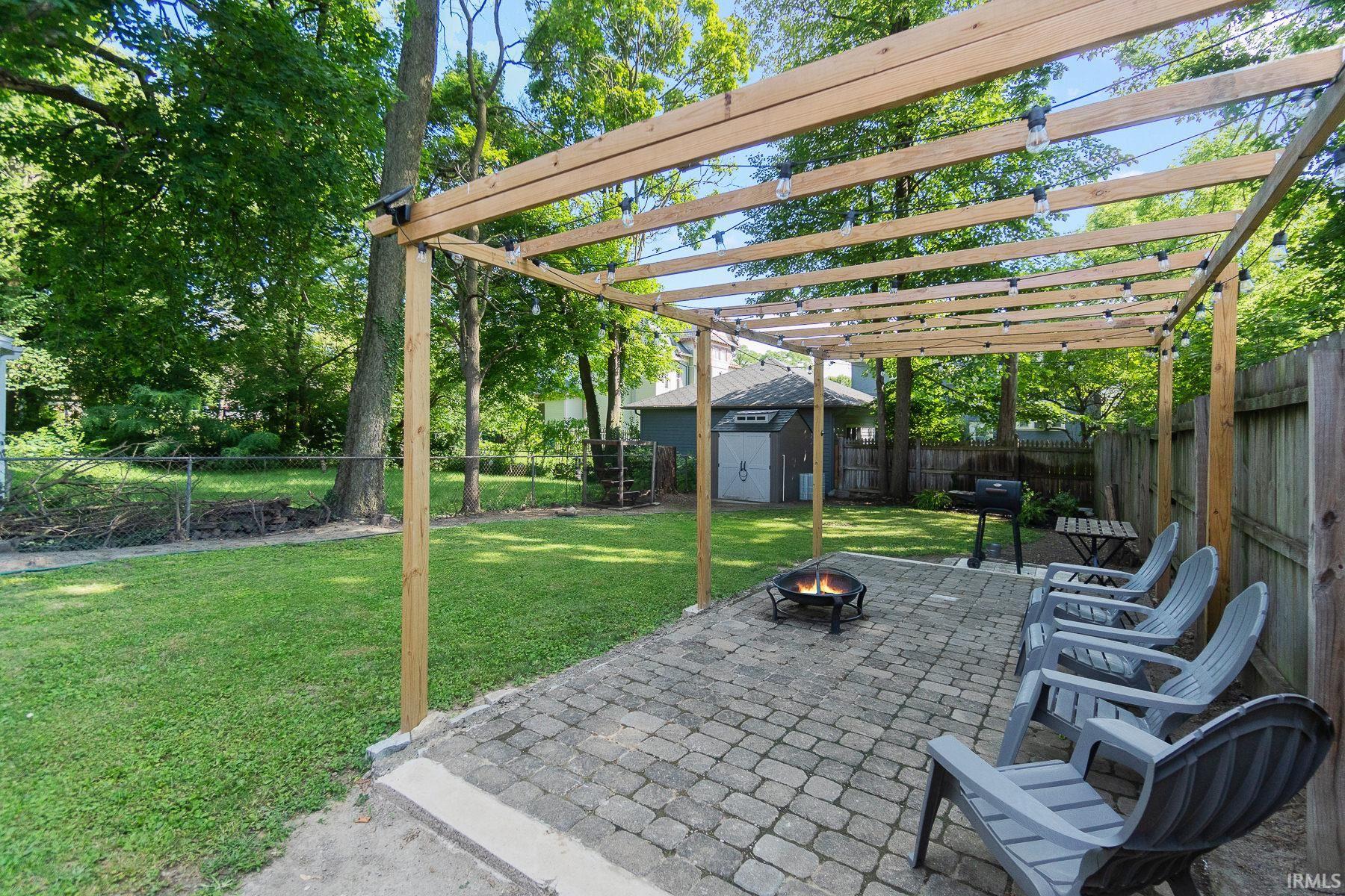 Fenced backyard featuring a shed, a fire pit, a patio area, area for grilling, and a pergola