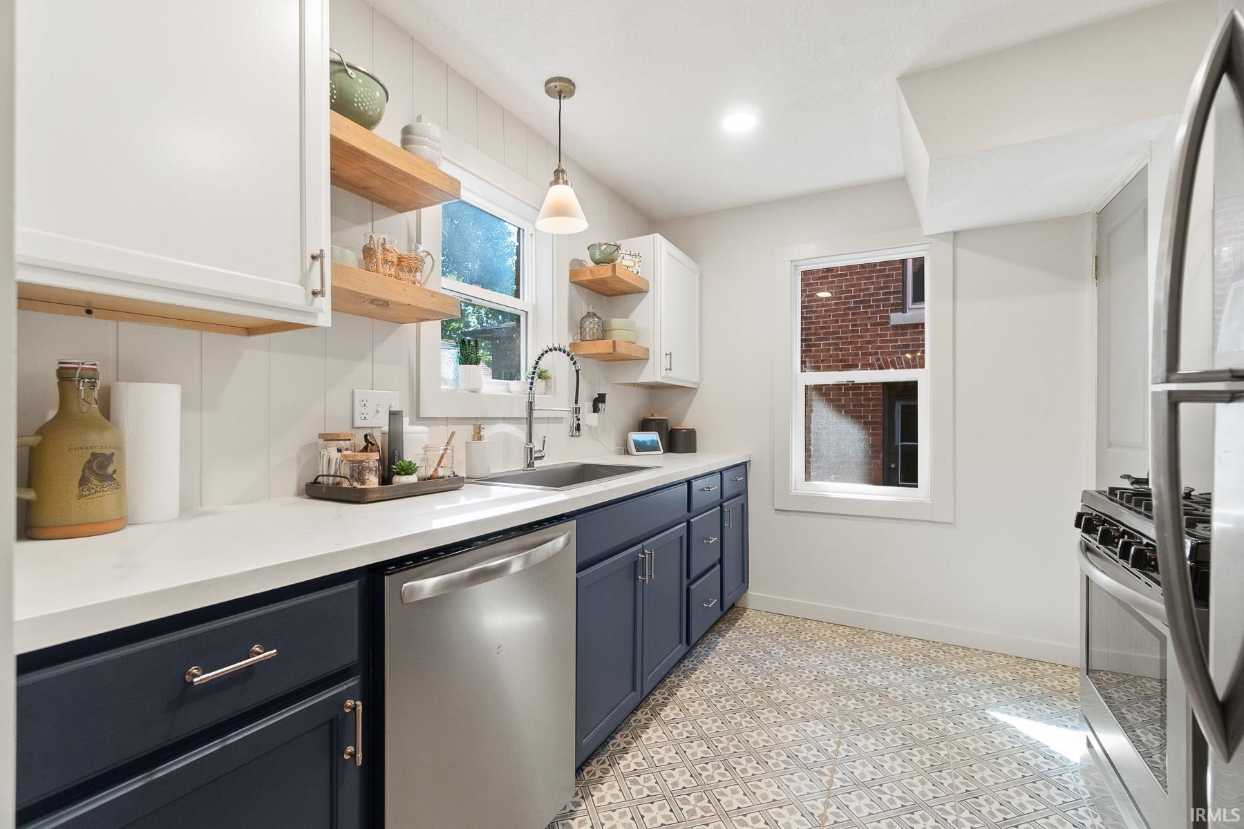 Kitchen featuring stainless steel appliances, dual tone cabinetry, open shelves, pendant lighting, and light floors