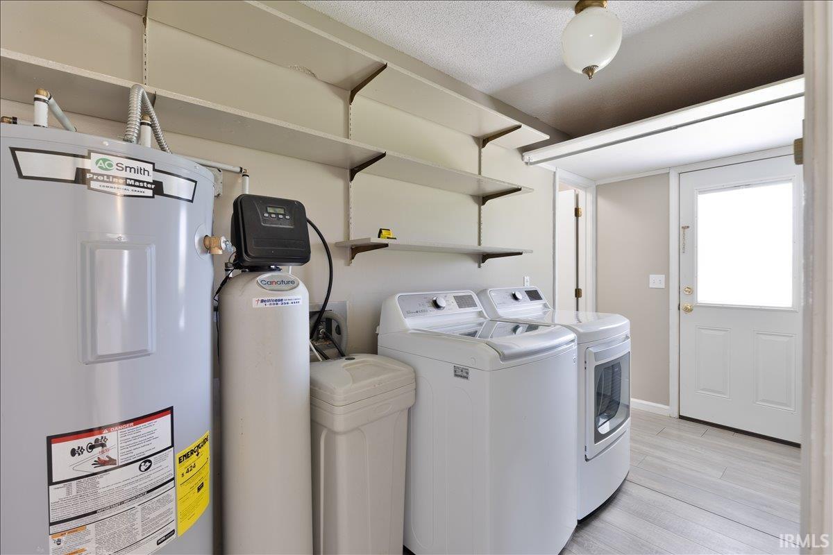 Laundry area featuring water heater, light wood finished floors, independent washer and dryer, and a textured ceiling