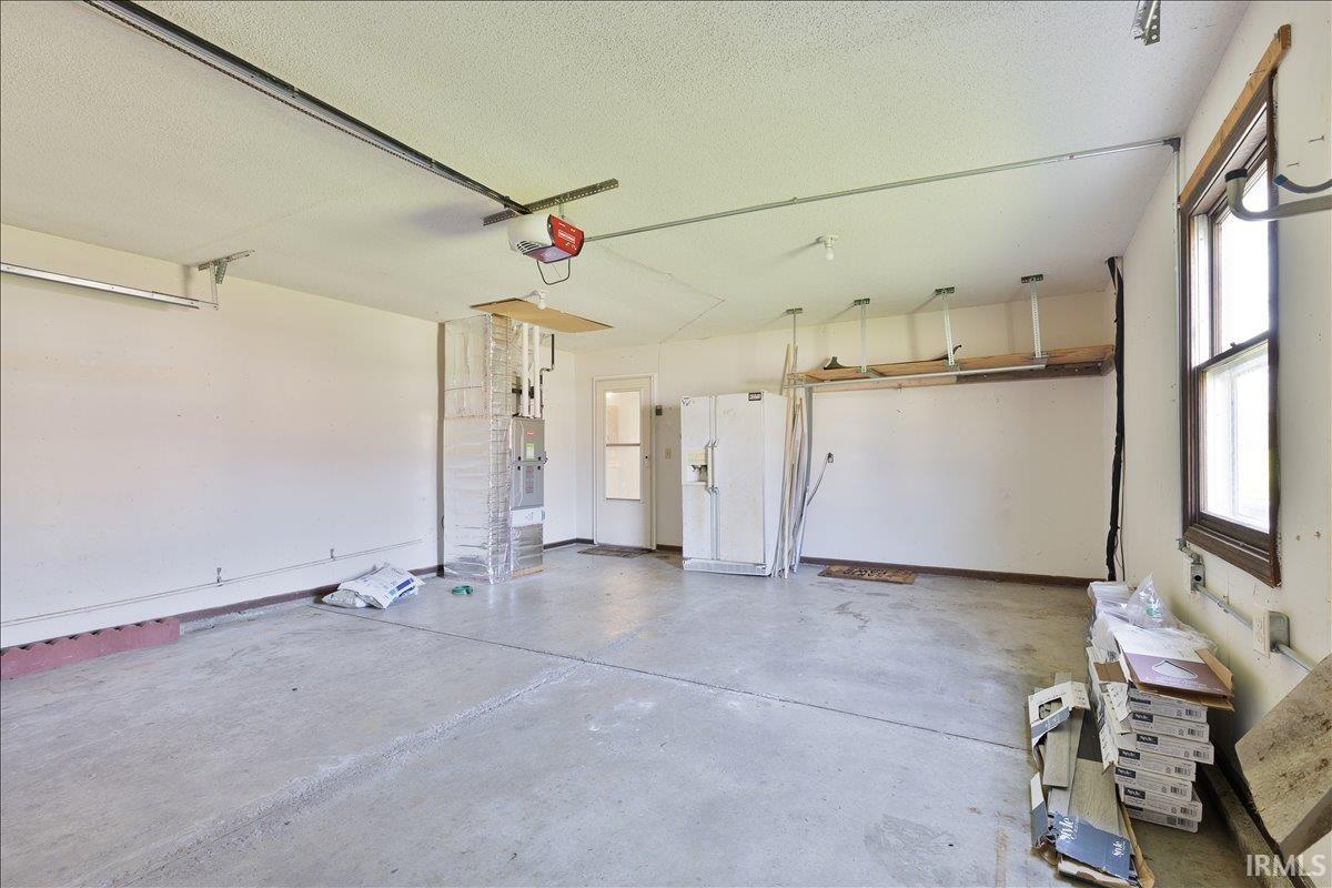 Garage with white refrigerator with ice dispenser, a garage door opener, and water heater
