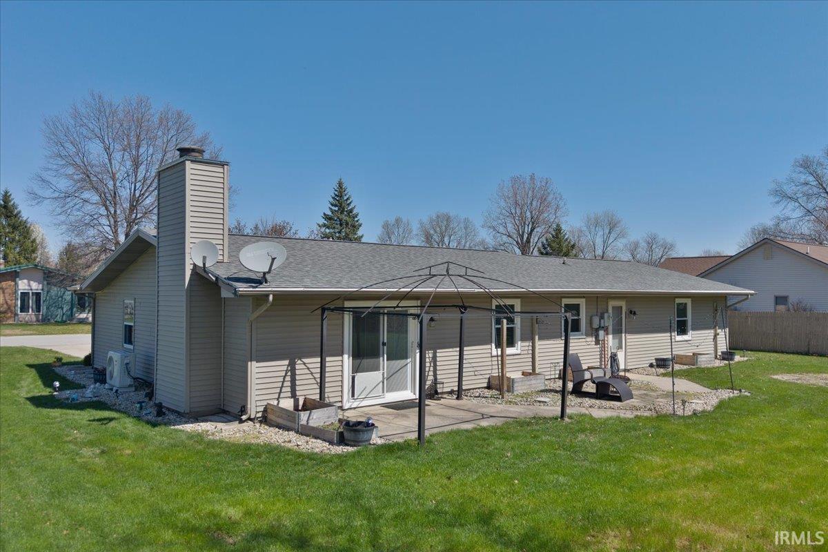 Back of house featuring a yard, a chimney, a patio area, and a shingled roof
