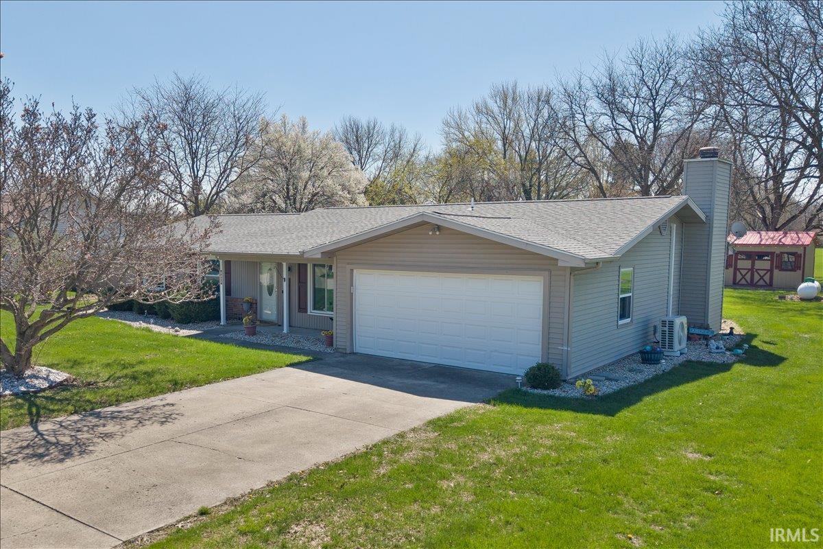 Ranch-style house featuring a front lawn, a chimney, an attached garage, roof with shingles, and driveway