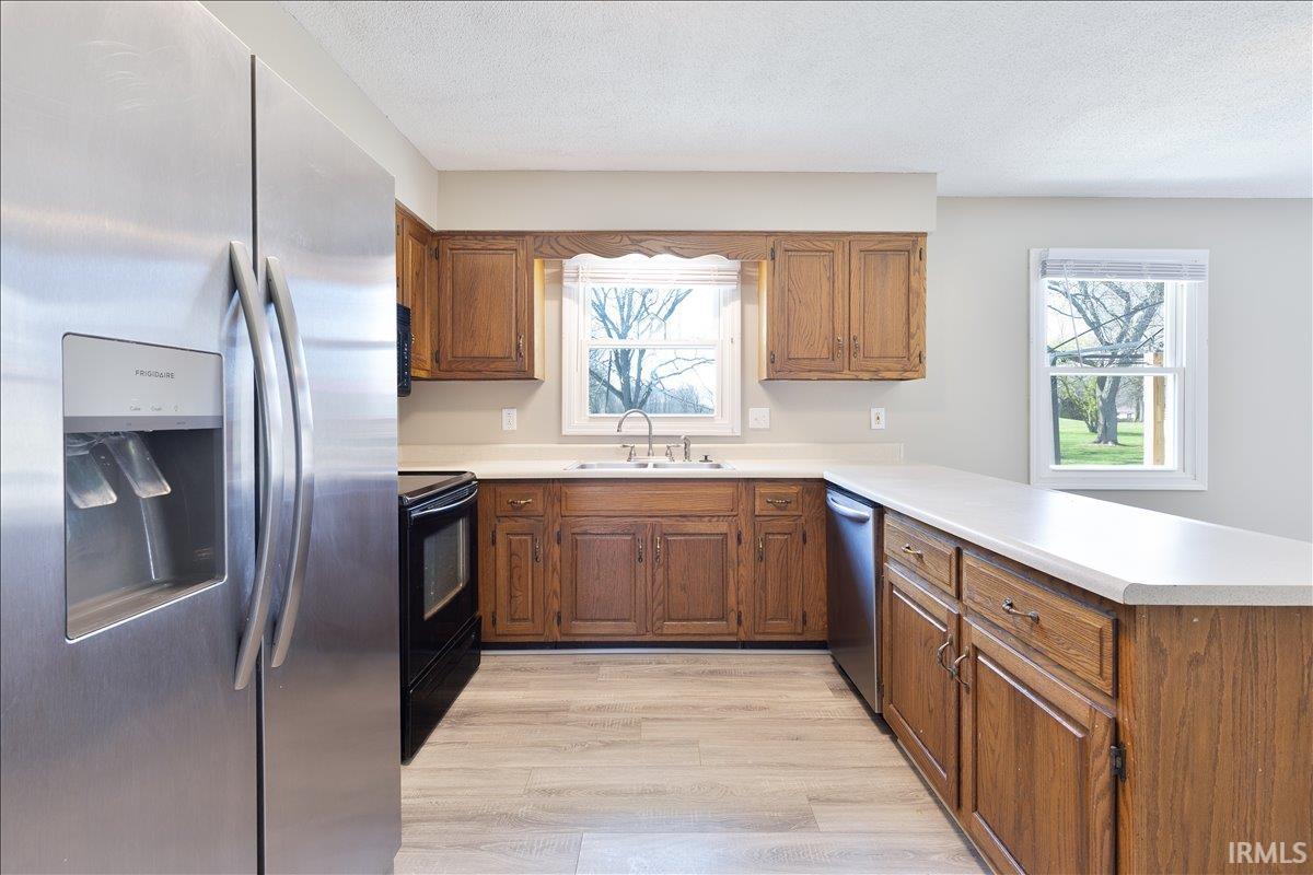 Kitchen with stainless steel appliances, wood finish cabinetry, light countertops, and a textured ceiling