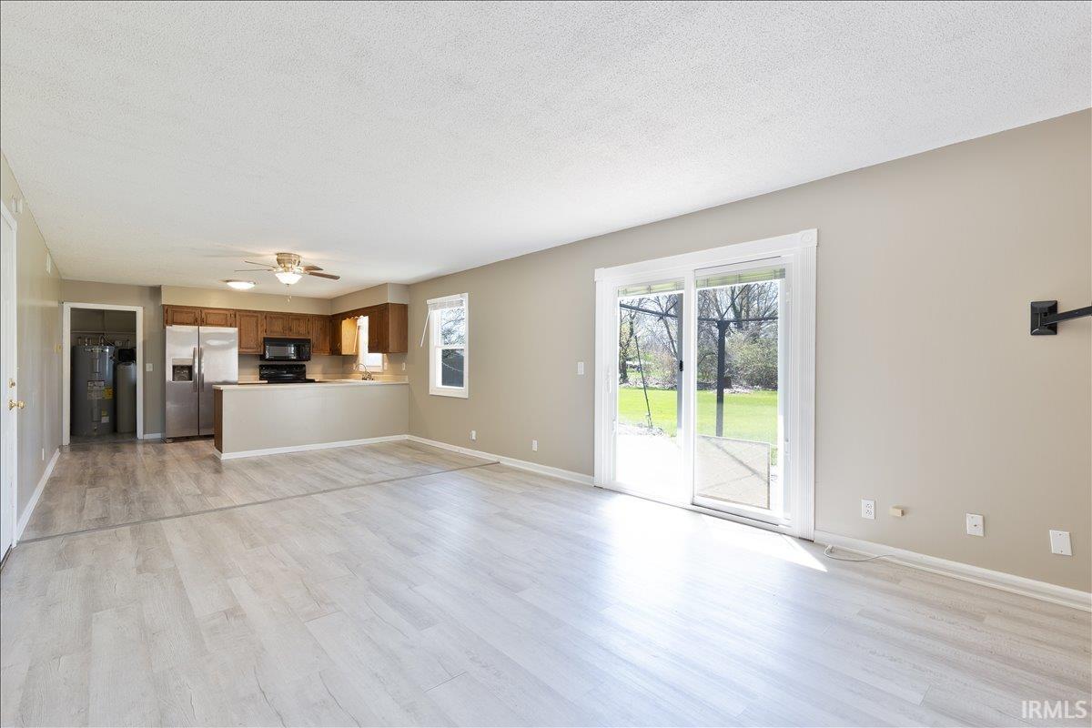 Unfurnished living room featuring light wood-style flooring, a textured ceiling, water heater, and a ceiling fan