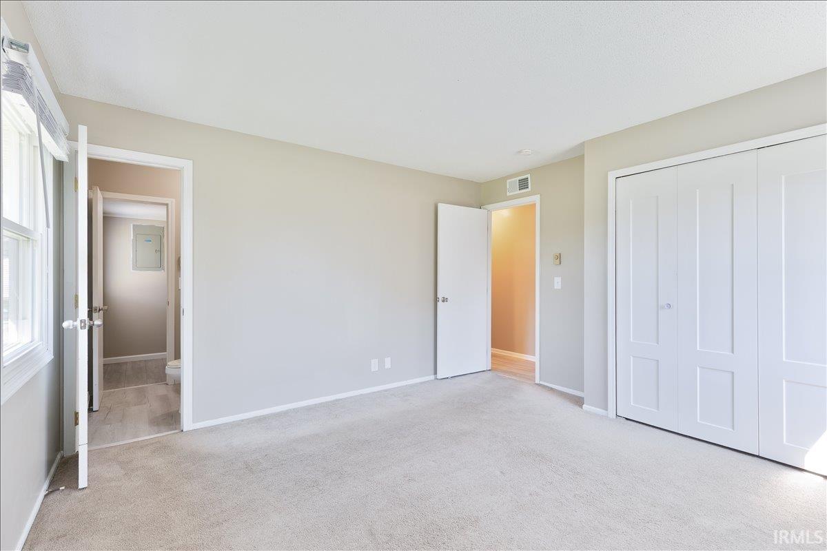 Unfurnished bedroom with light carpet, a closet, and electric panel