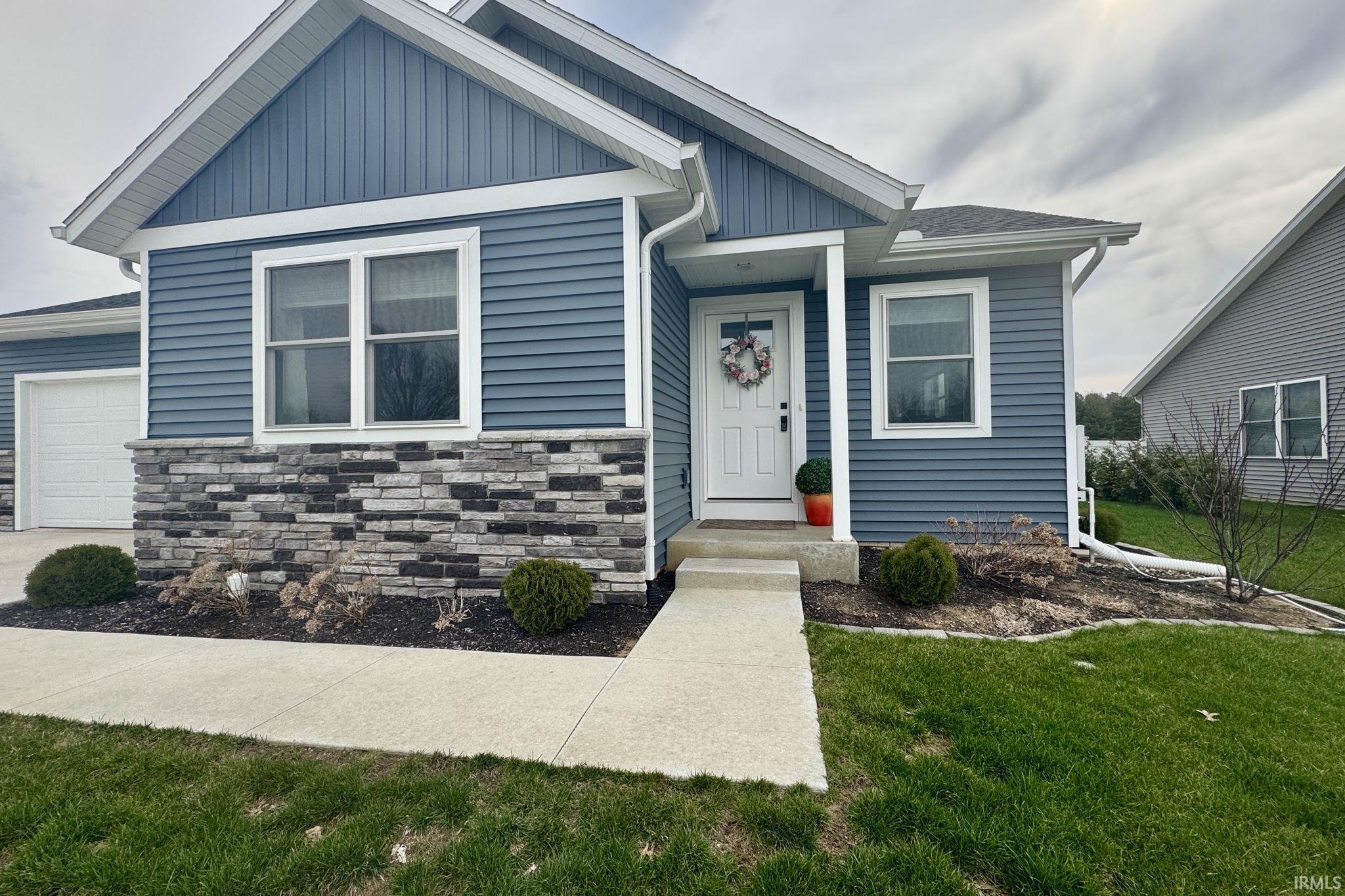 View of front of property with a front yard, stone siding, a garage, and board and batten siding