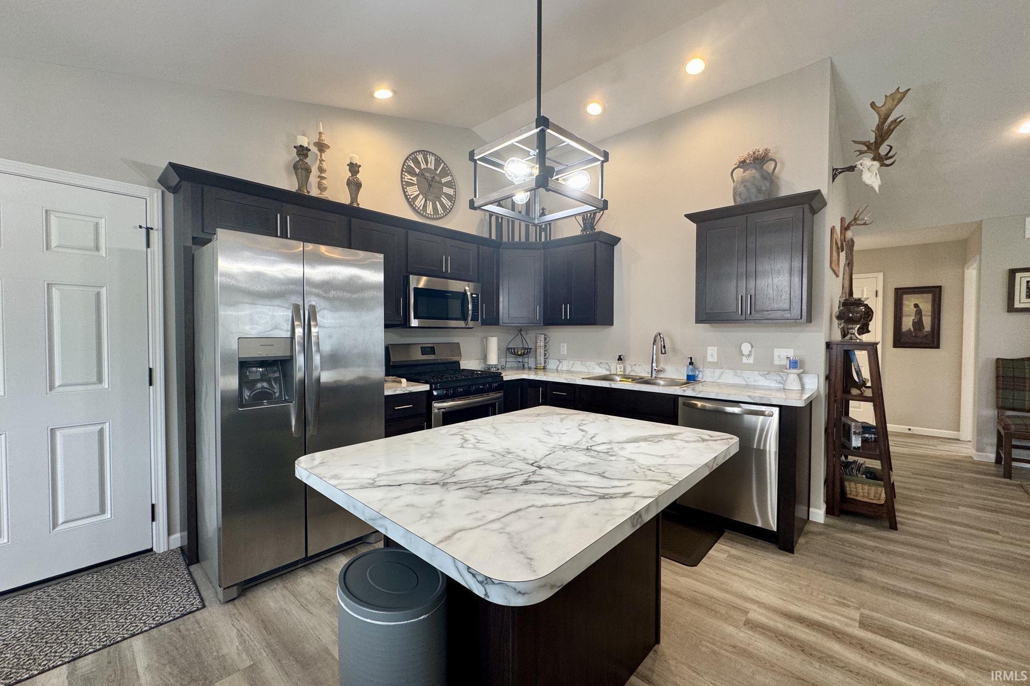 Kitchen with stainless steel appliances, light countertops, light wood-type flooring, a kitchen island, and a high ceiling