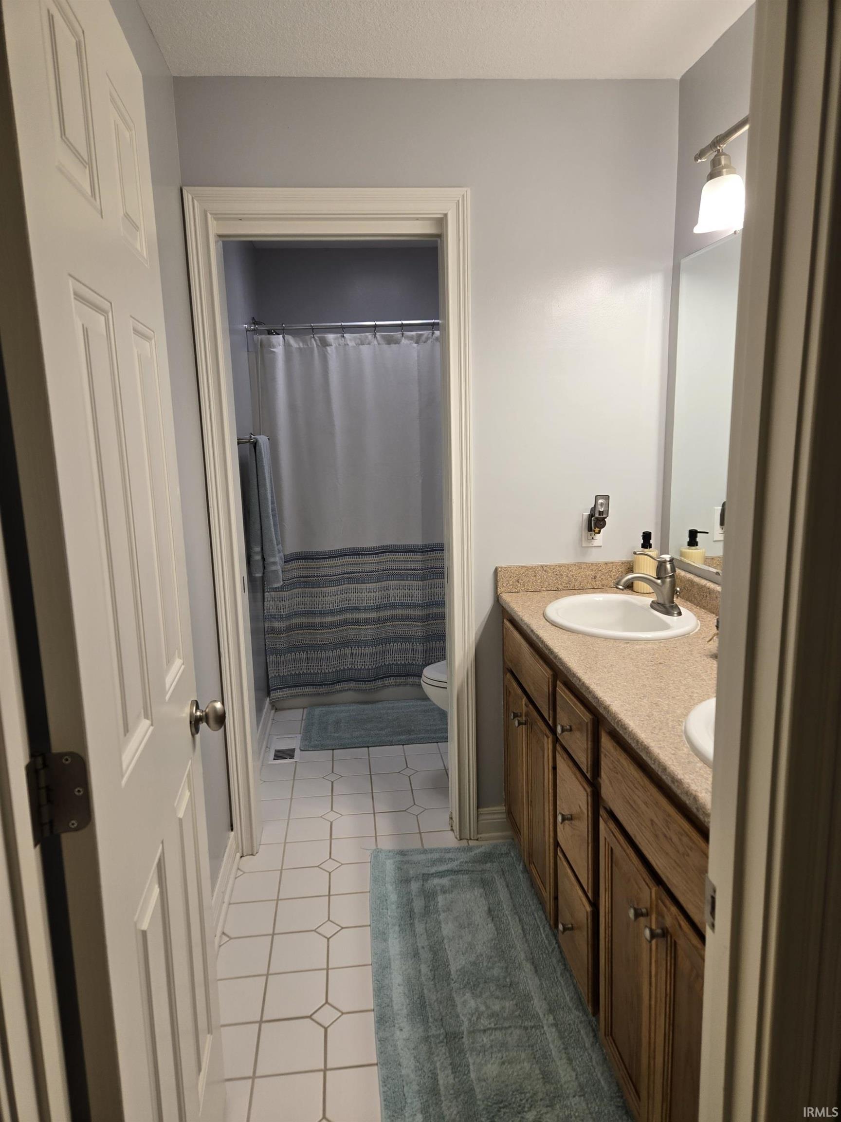 Full bath featuring double vanity, curtained shower, light tile patterned floors, and a textured ceiling