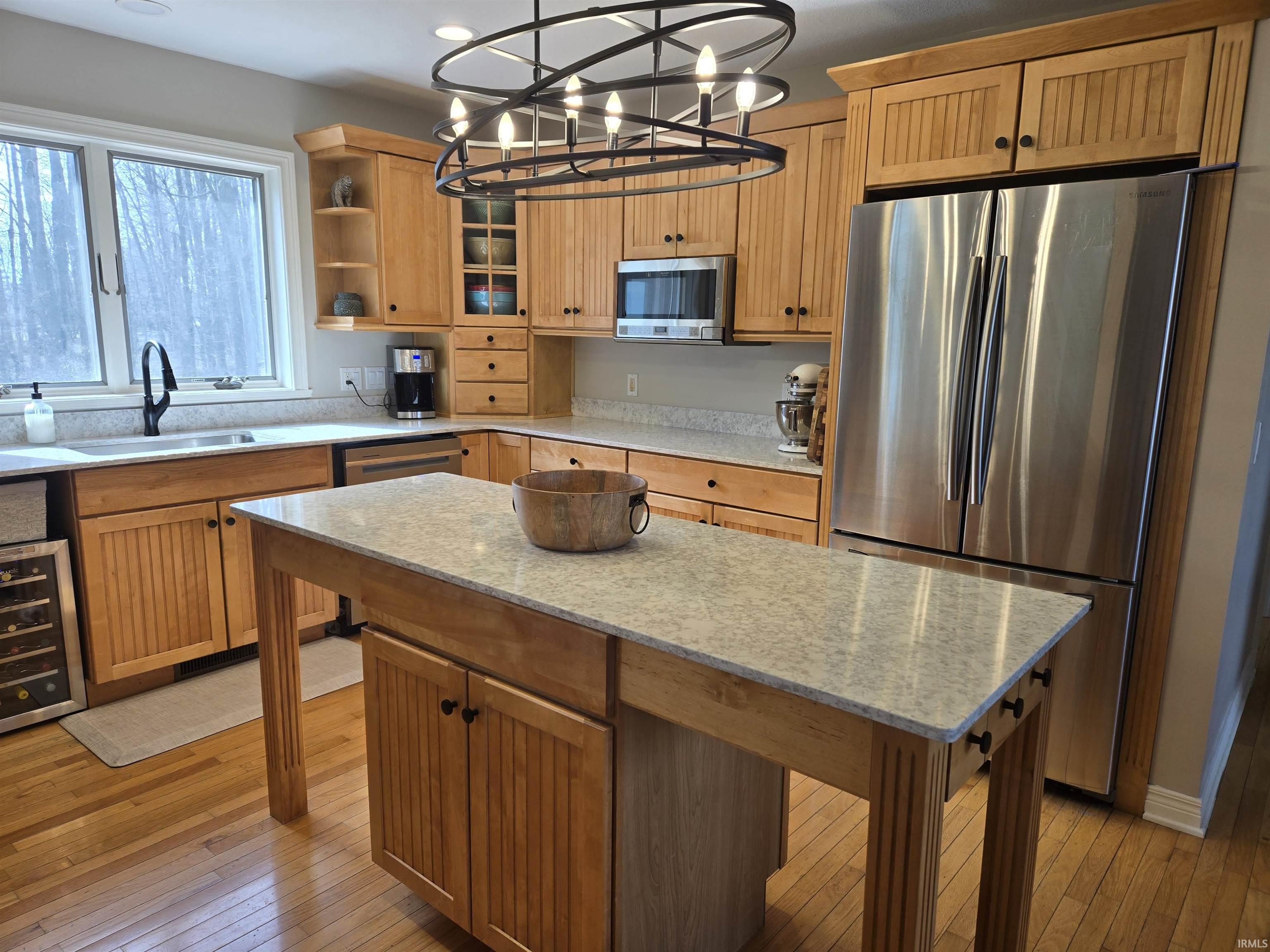 Kitchen with stainless steel appliances, light wood finished floors, beverage cooler, light stone countertops, and open shelves