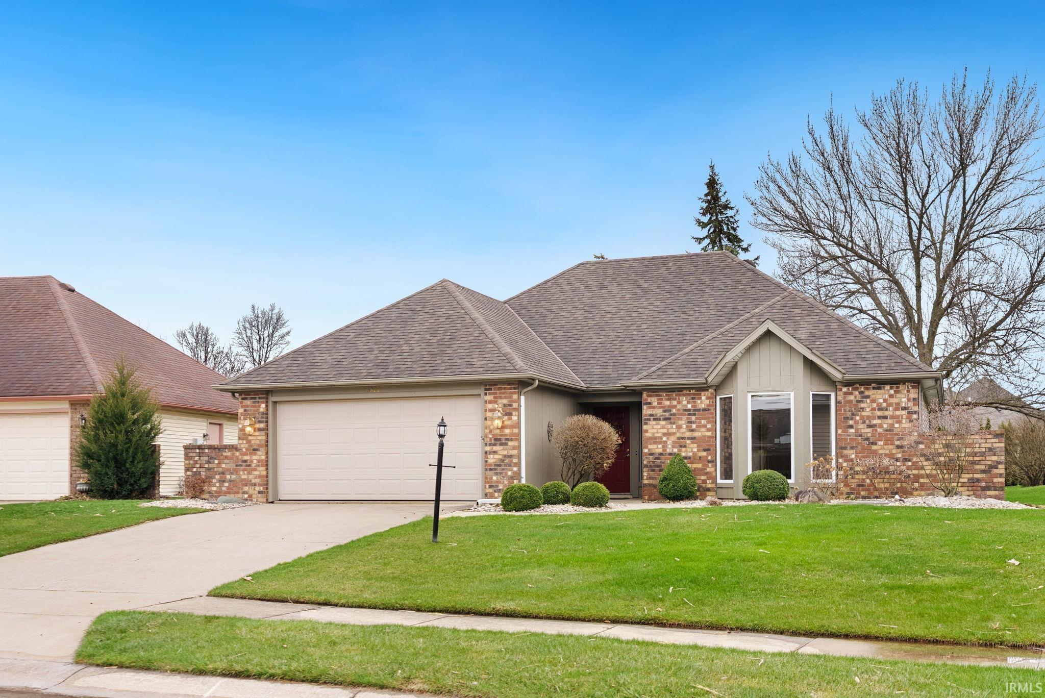 Ranch-style house featuring a shingled roof, a front yard, an attached garage, brick siding, and concrete driveway