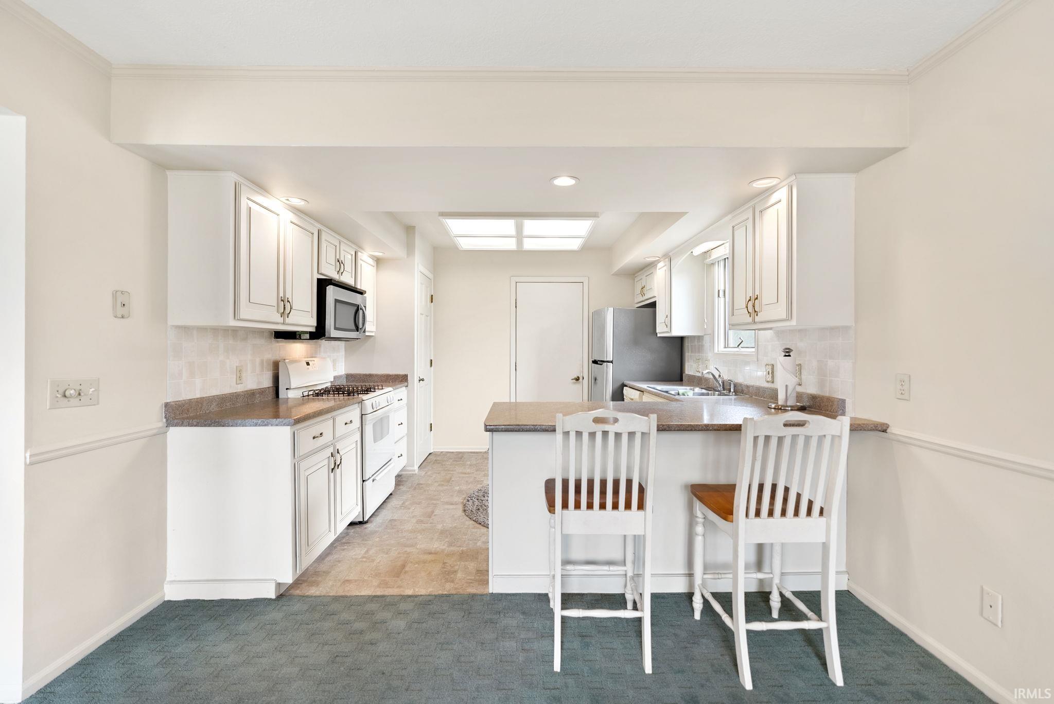 Kitchen with decorative backsplash, a breakfast bar, white cabinets, and recessed lighting