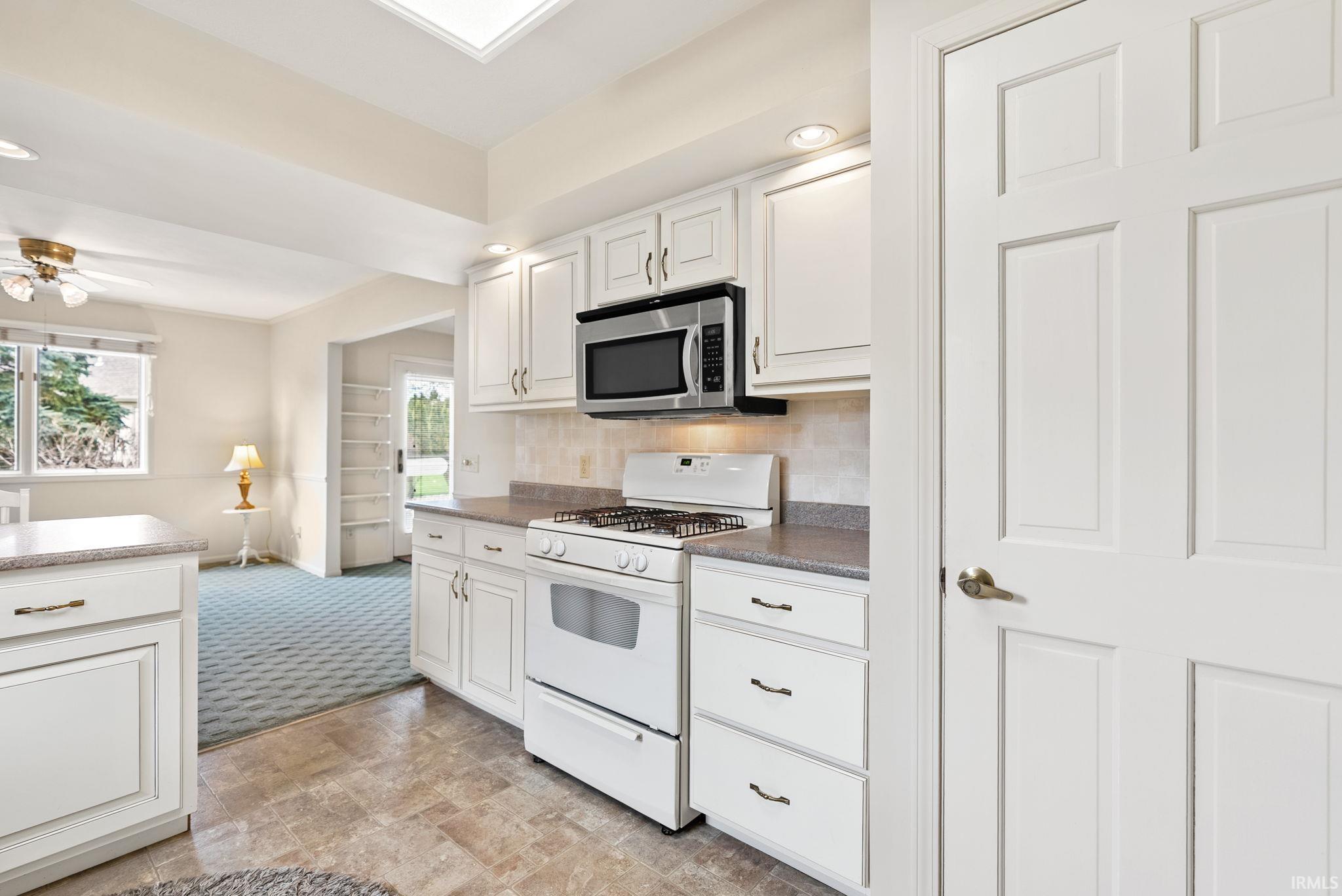 Kitchen with white gas range, white cabinets, decorative backsplash, stainless steel microwave, and stone finish flooring