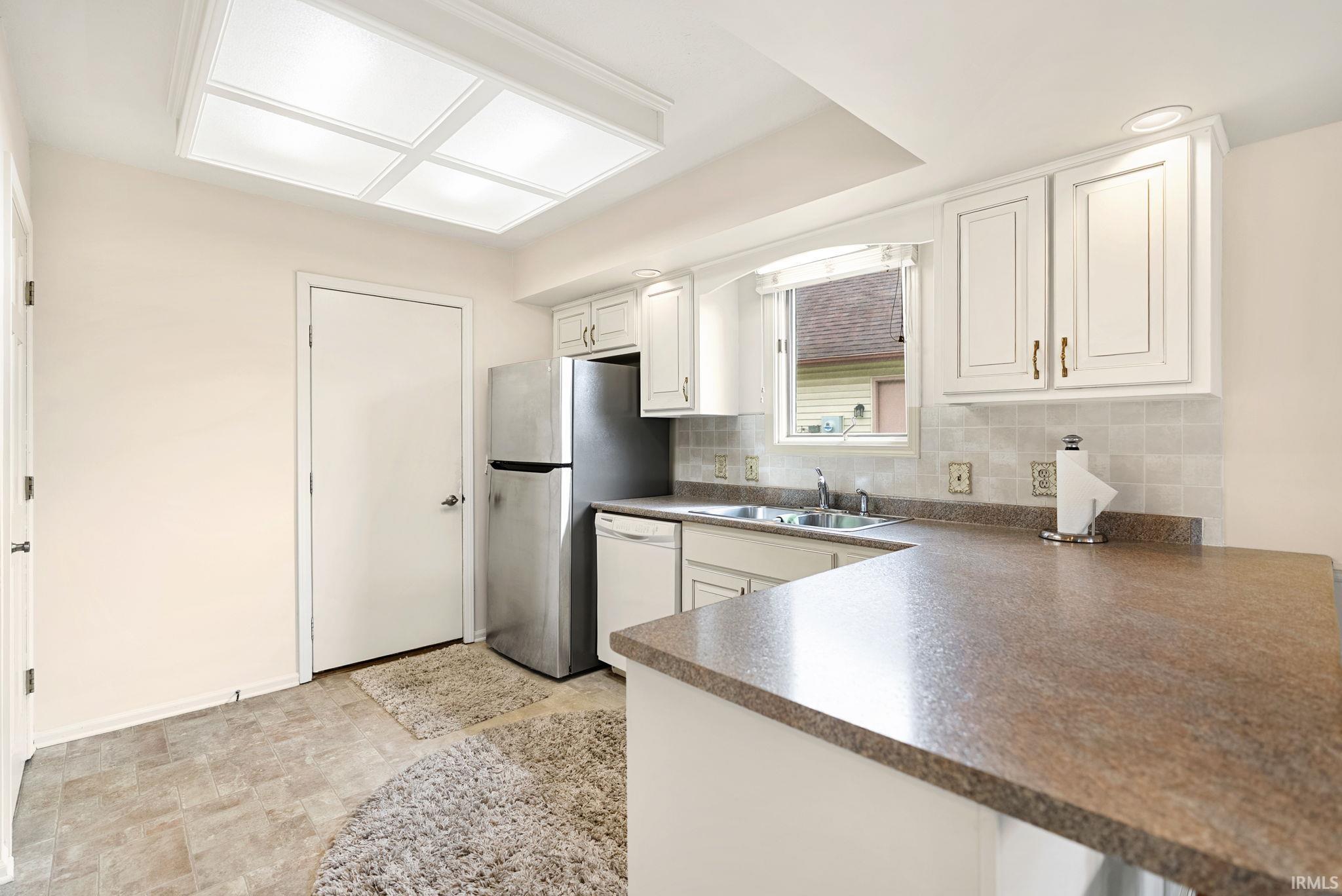 Kitchen with white cabinetry, dark countertops, stone finish floors, white dishwasher, and a peninsula