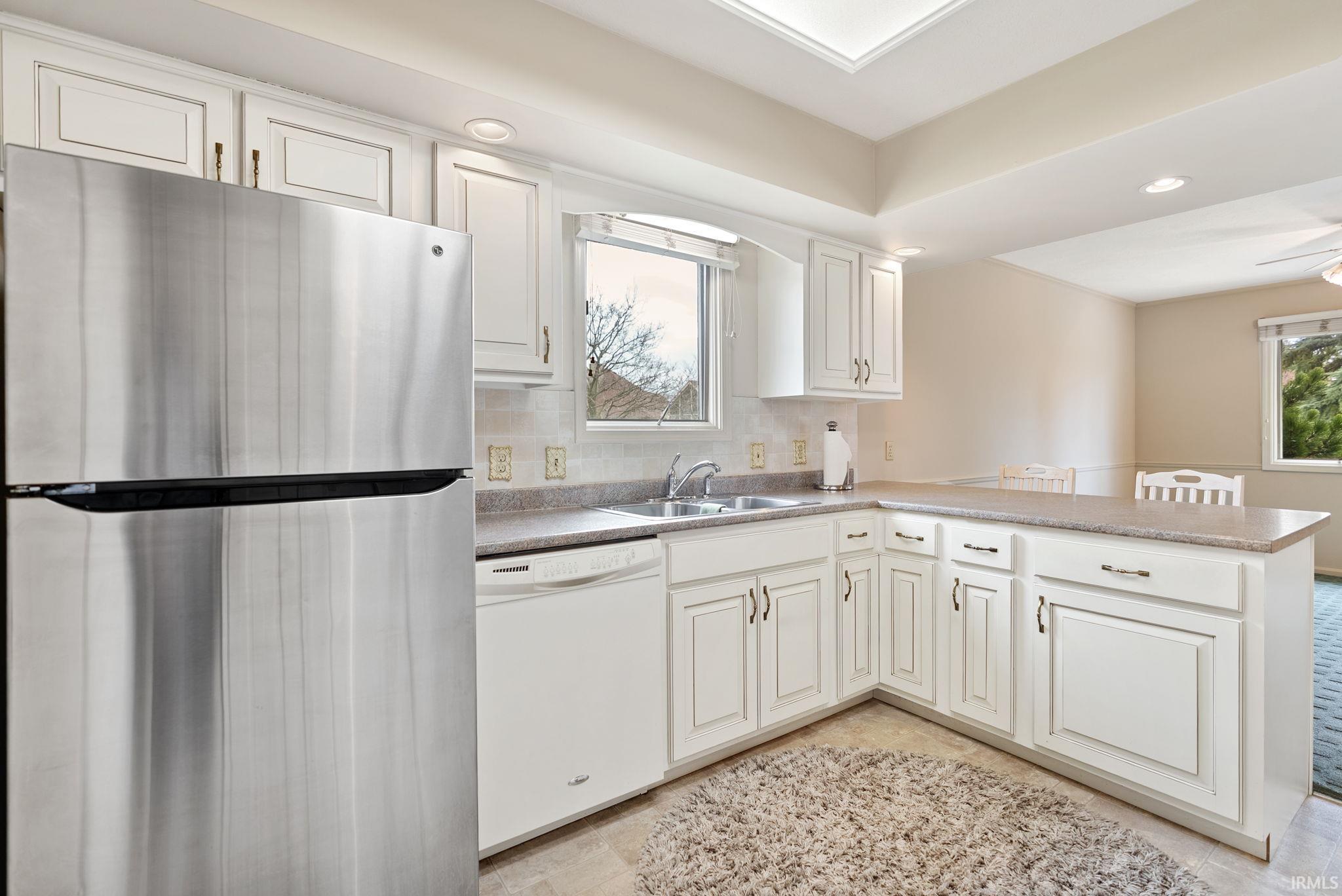 Kitchen with freestanding refrigerator, a peninsula, dishwasher, decorative backsplash, and recessed lighting