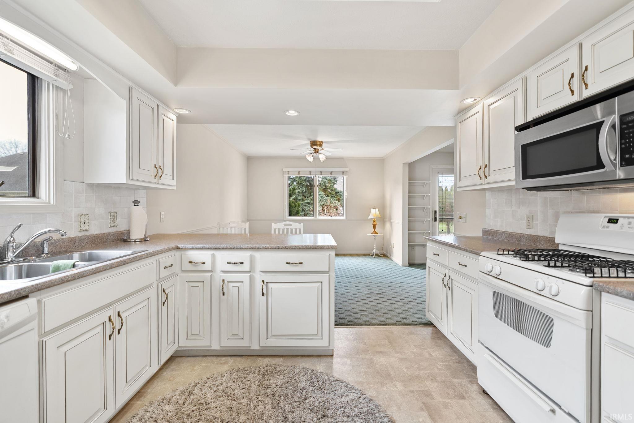 Kitchen featuring backsplash, white appliances, a peninsula, white cabinetry, and recessed lighting