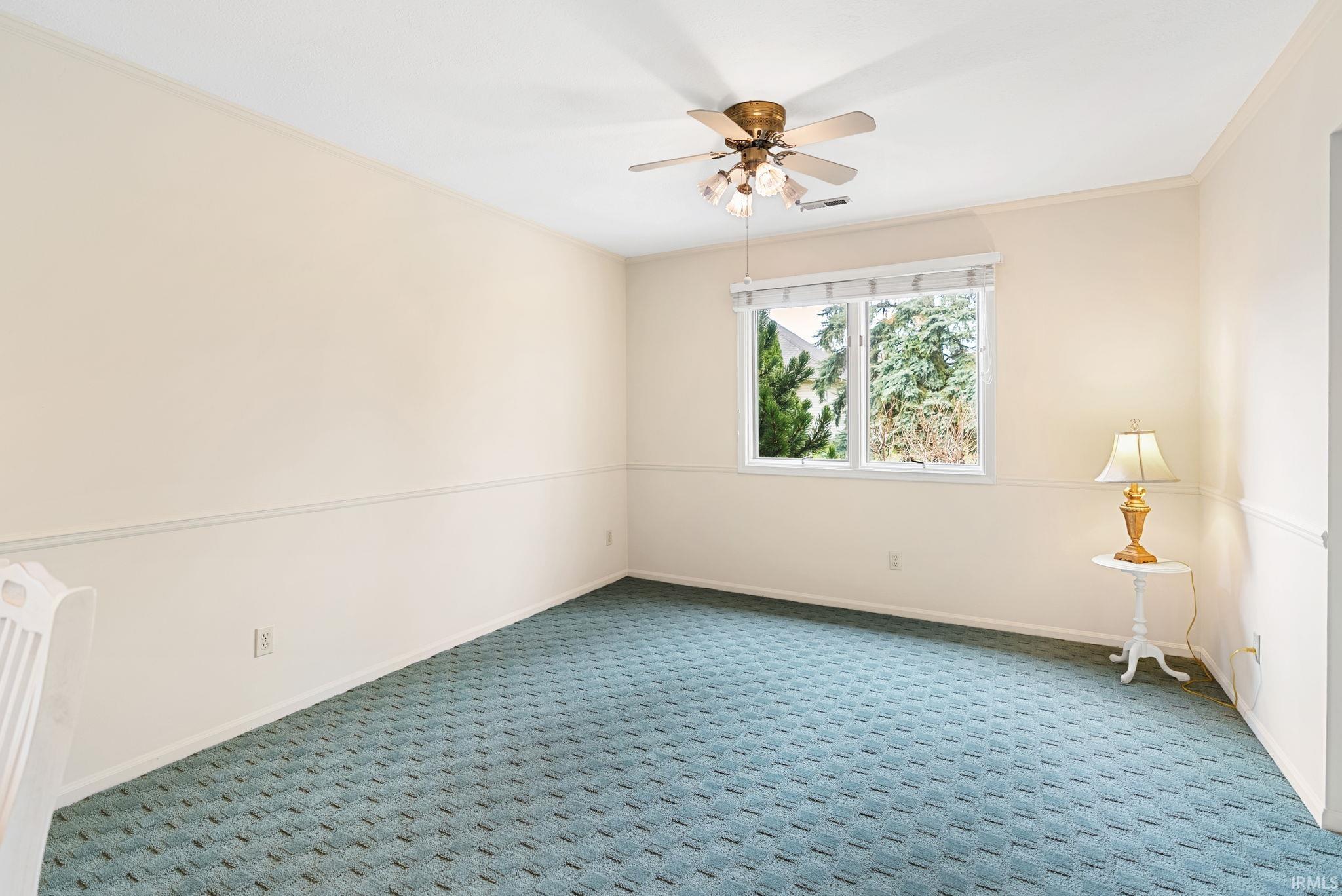 Carpeted empty room with ornamental molding and a ceiling fan