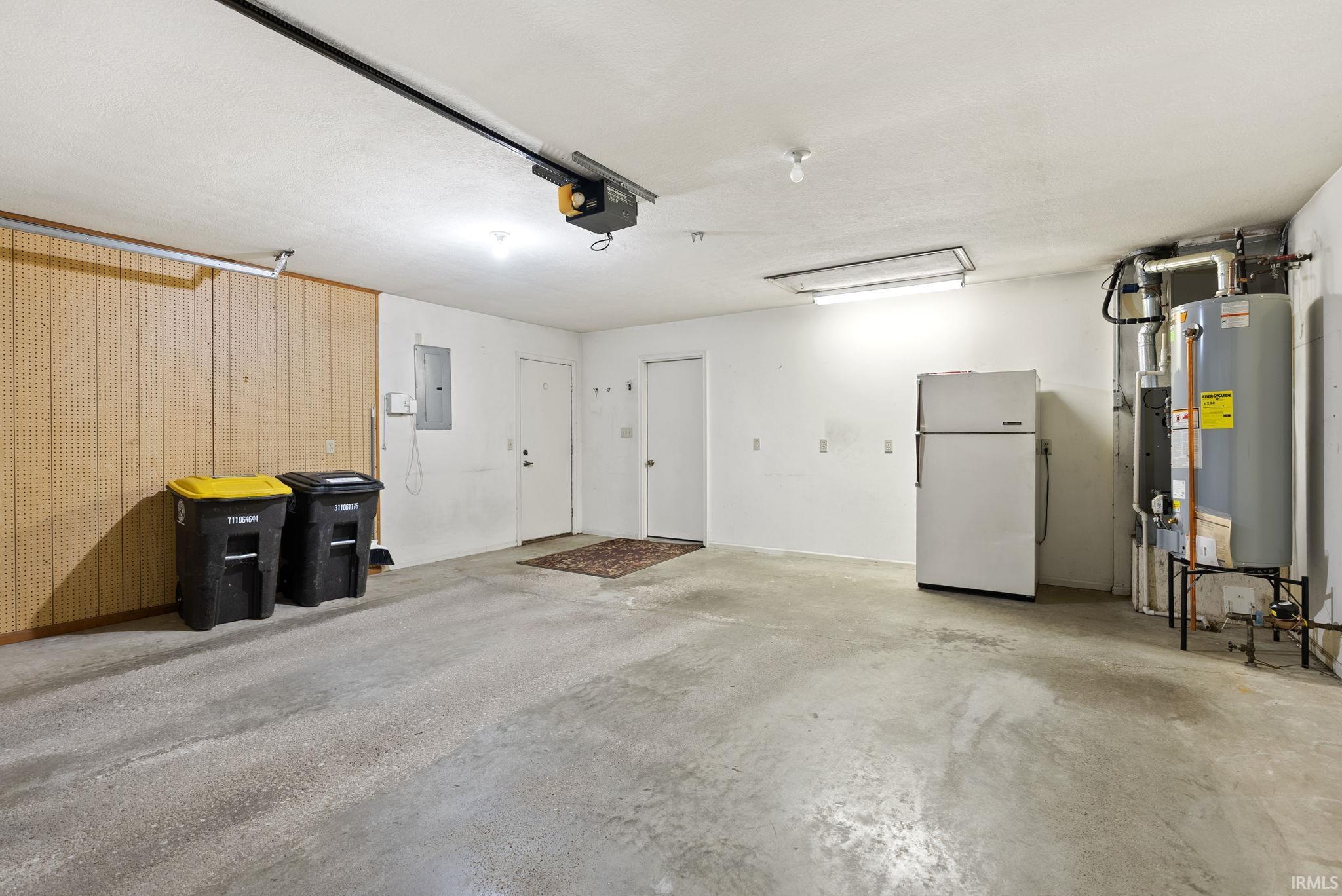 Garage featuring freestanding refrigerator, water heater, electric panel, and a garage door opener