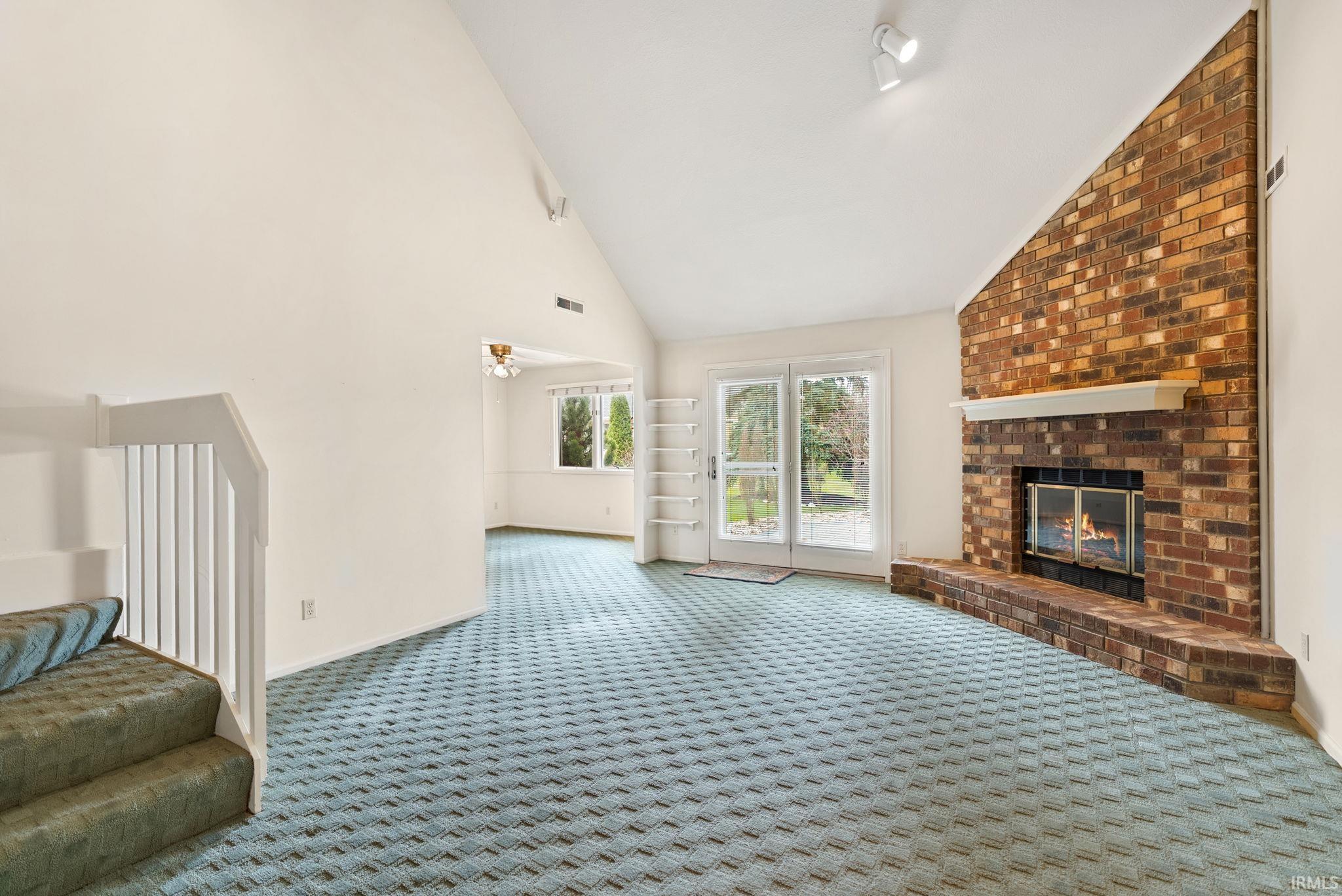 Unfurnished living room with lofted ceiling, a fireplace, and carpet flooring