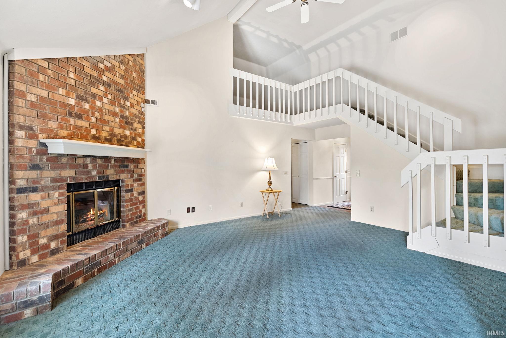 Unfurnished living room with a fireplace, lofted ceiling, ceiling fan, and carpet