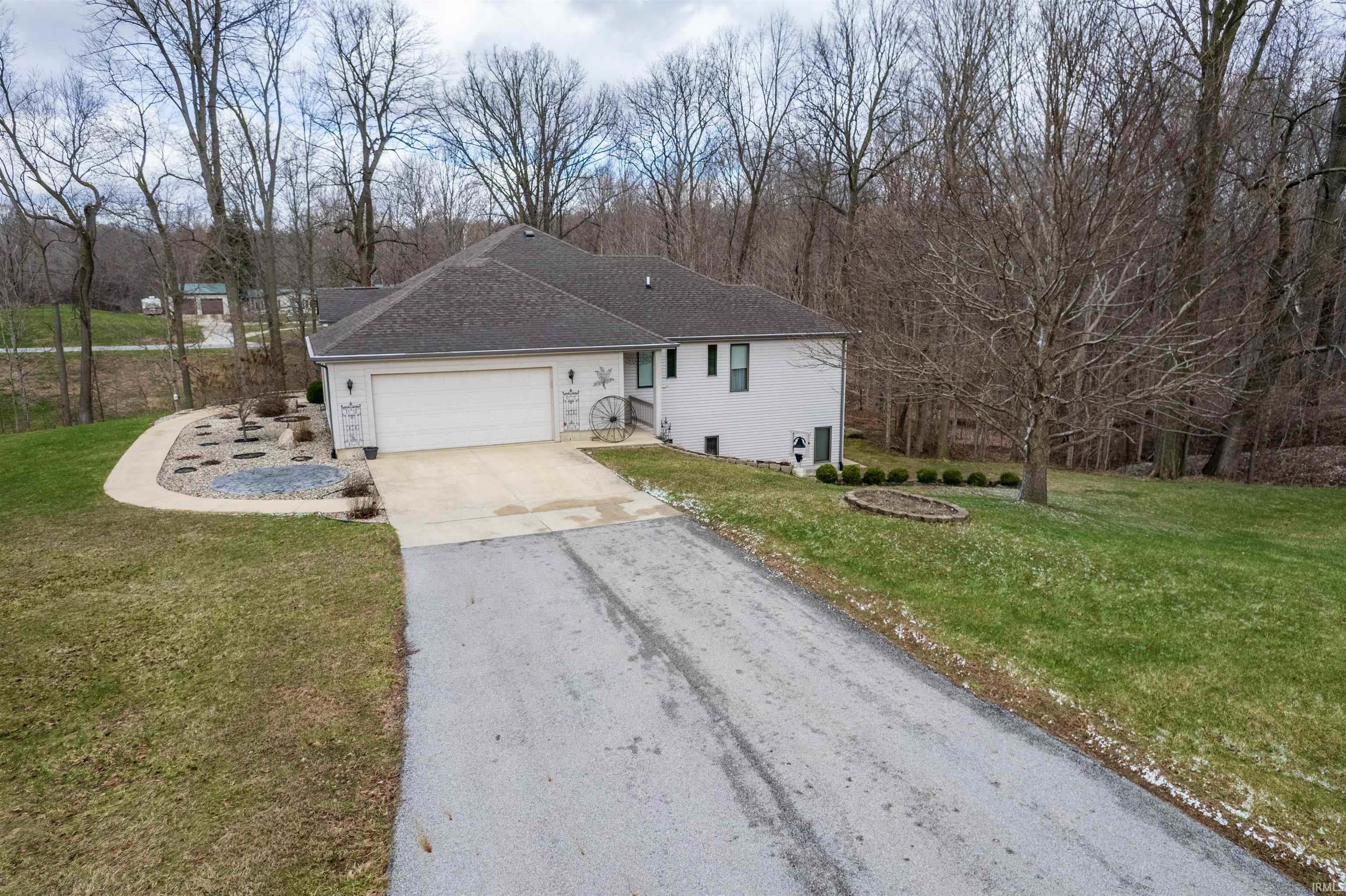 Ranch-style home featuring driveway, a front yard, a garage, and view of scattered trees