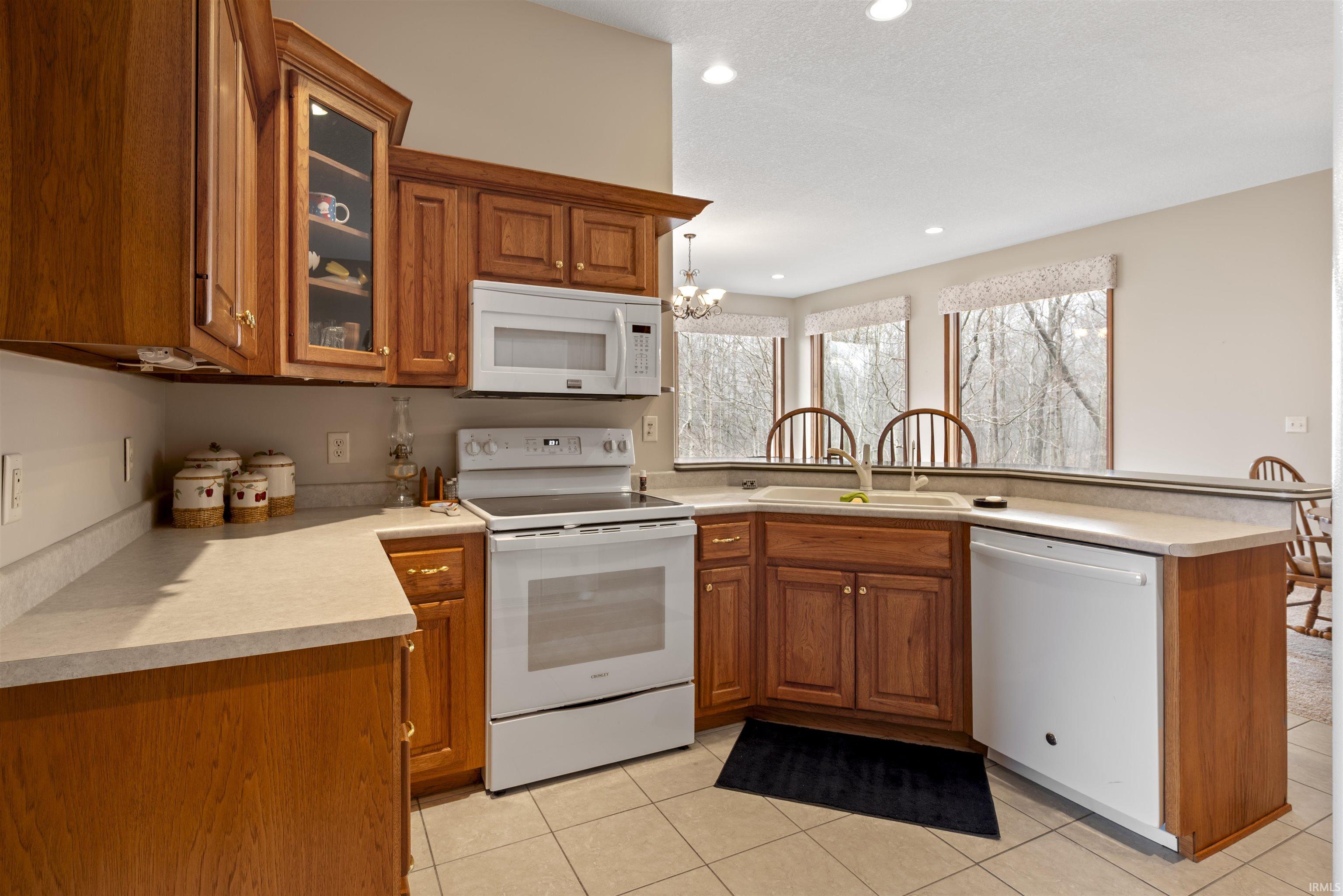 Kitchen with wood finish cabinets, white appliances, a peninsula, glass fronted cabinets, and light countertops