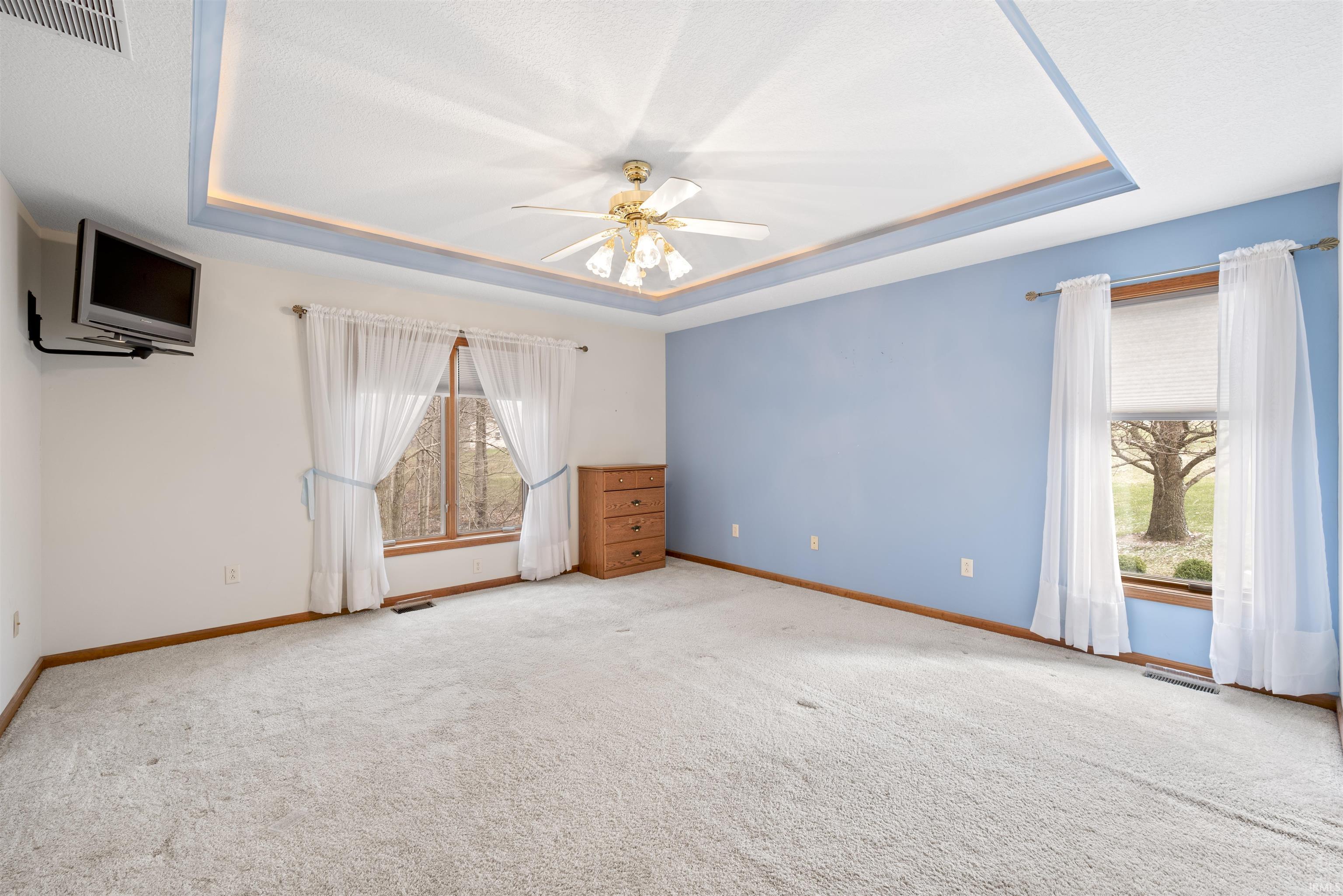 Carpeted spare room featuring a tray ceiling and ceiling fan