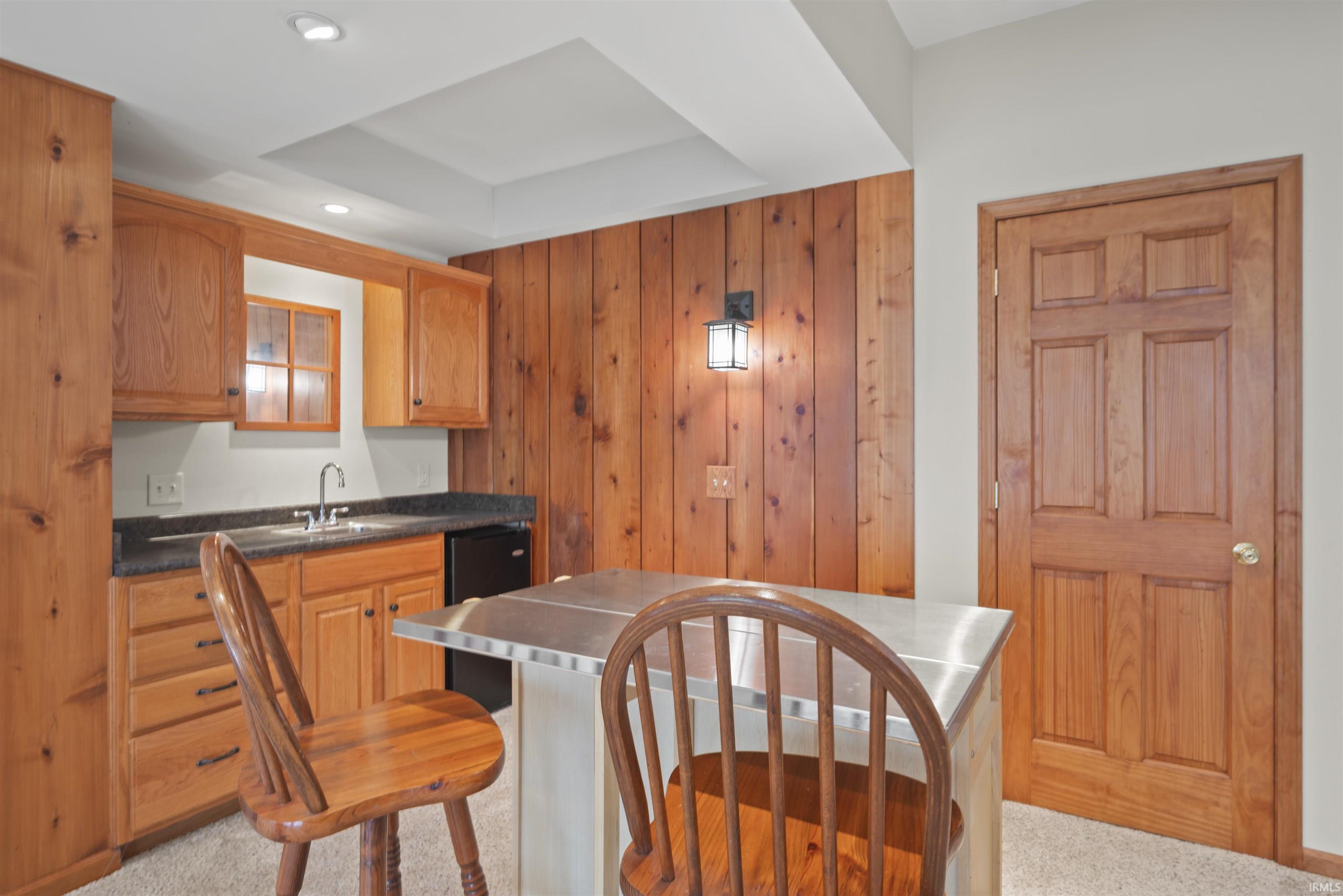 Kitchen with wooden walls, stainless steel countertops, dishwashing machine, light carpet, and a raised ceiling
