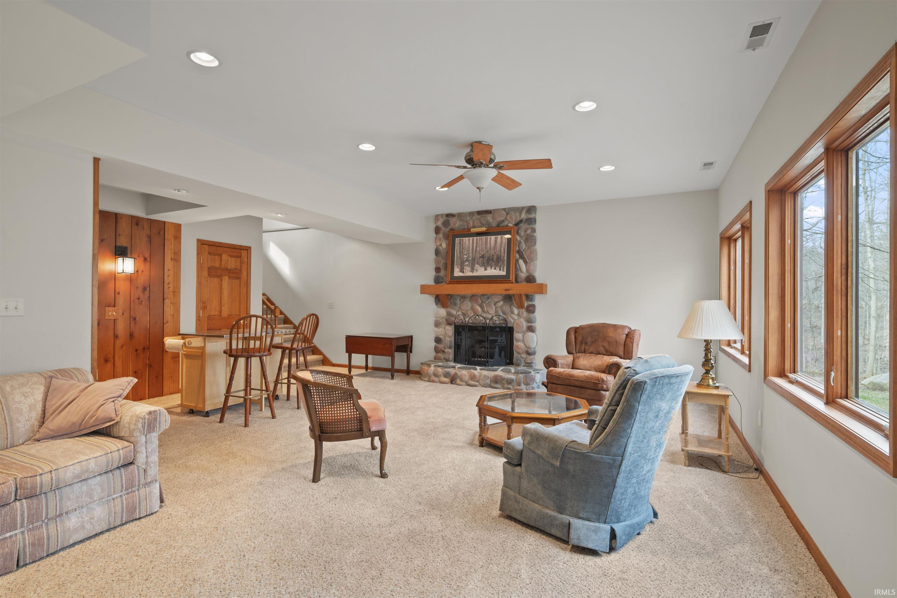 Living room with a ceiling fan, light colored carpet, recessed lighting, a stone fireplace, and wooden walls