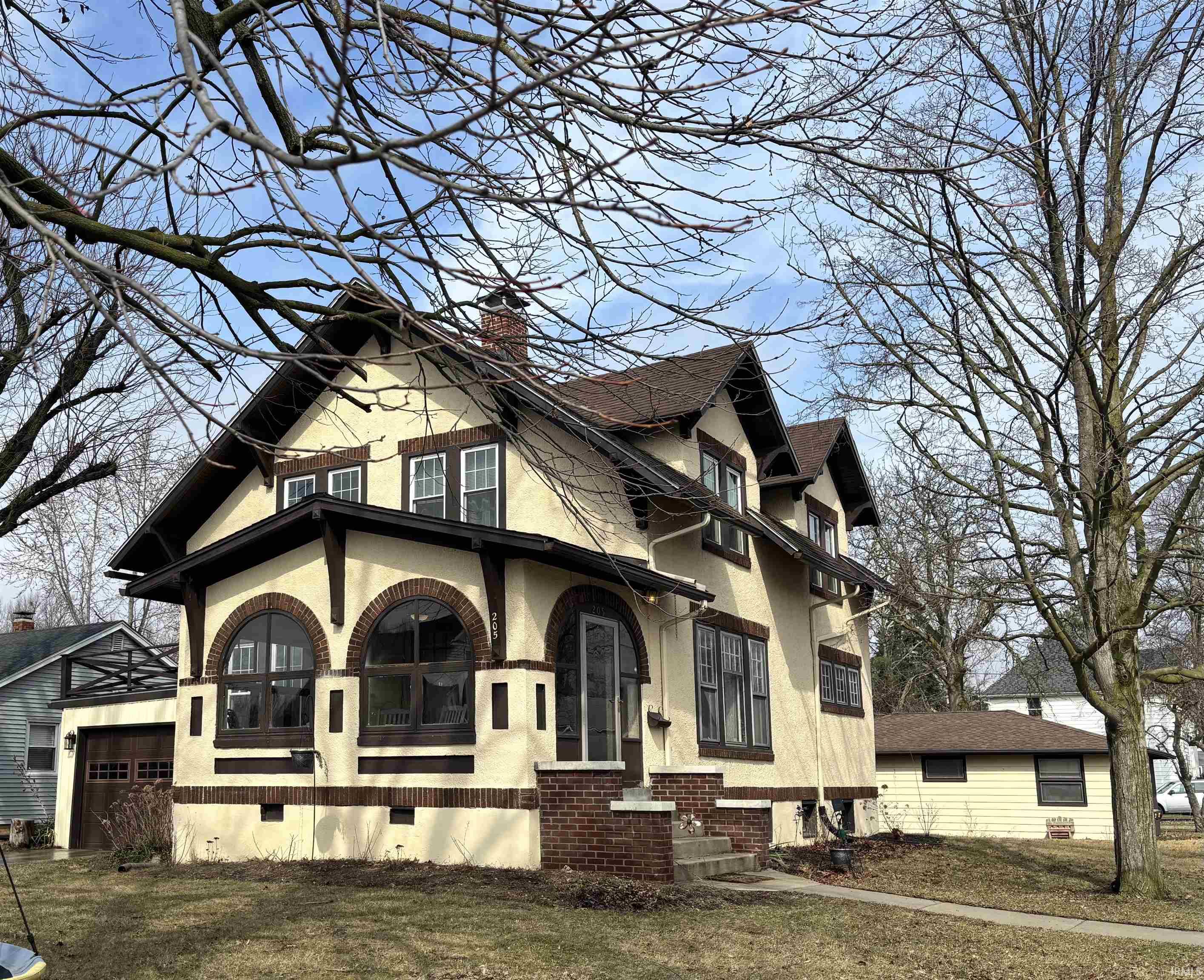 View of home's exterior featuring stucco siding, a chimney, covered porch, a garage, and brick siding